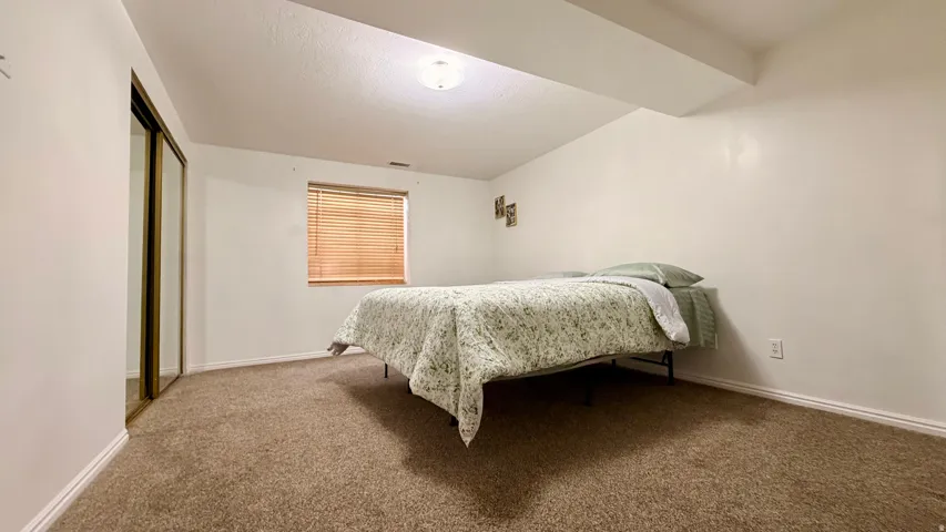 Carpeted room featuring a window with horizontal blinds, overhead lighting, and mirrored closet doors