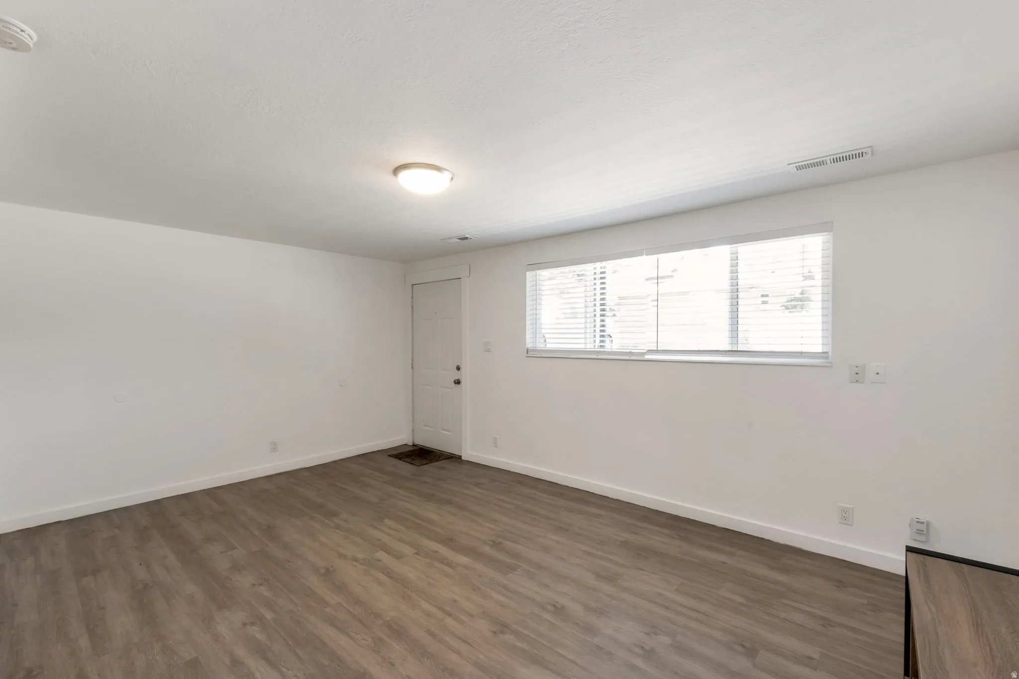Spacious room featuring wood-finish flooring, white baseboards, and a neutral wall palette