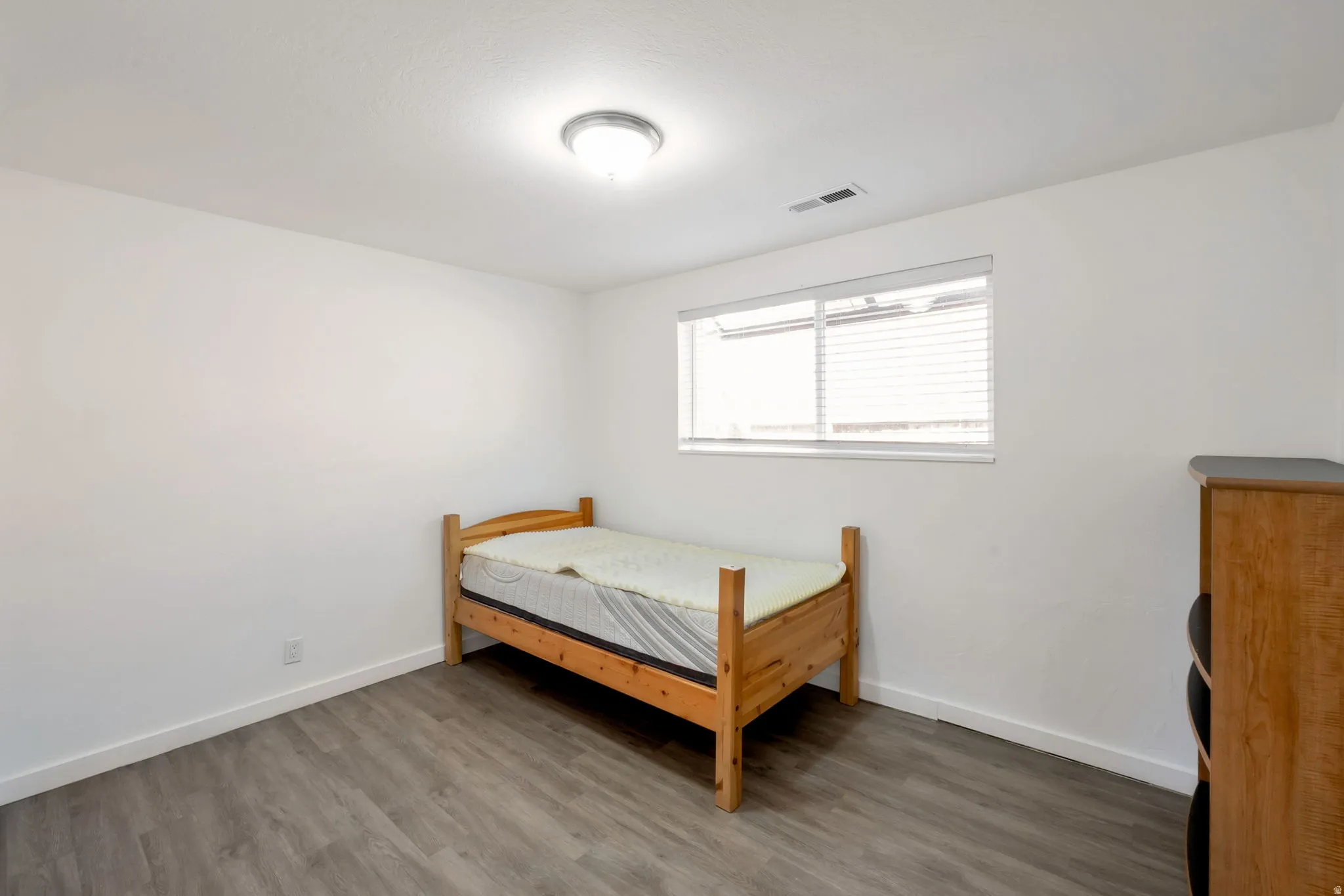 Bright room featuring wood-finish flooring, white walls, and a single window with blinds