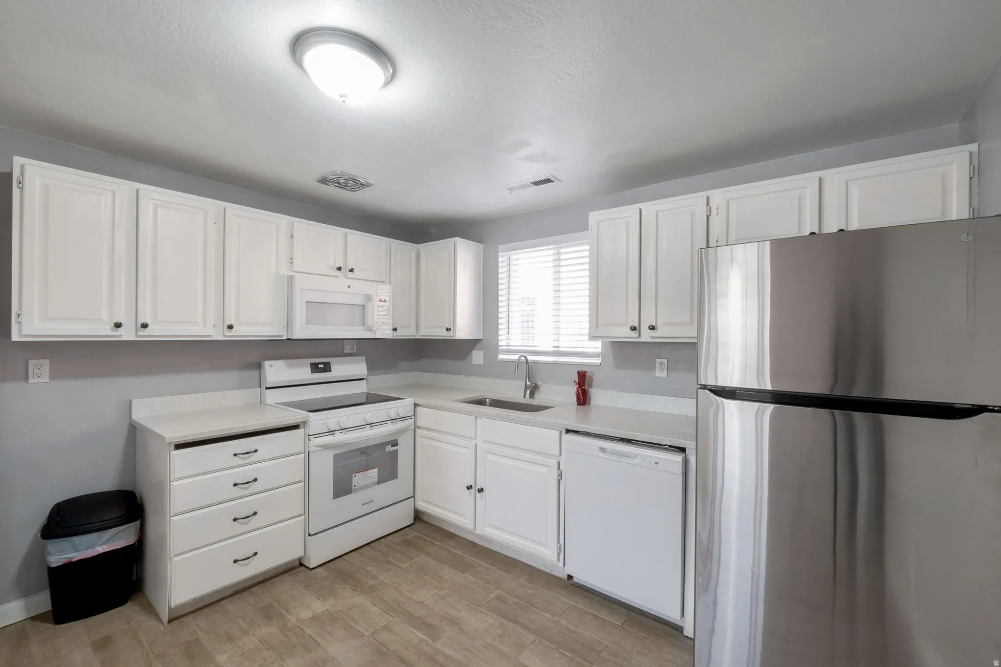 Kitchen featuring white cabinetry, light-toned countertops, wood-finish flooring, a stainless steel refrigerator, and an over-the-range microwave