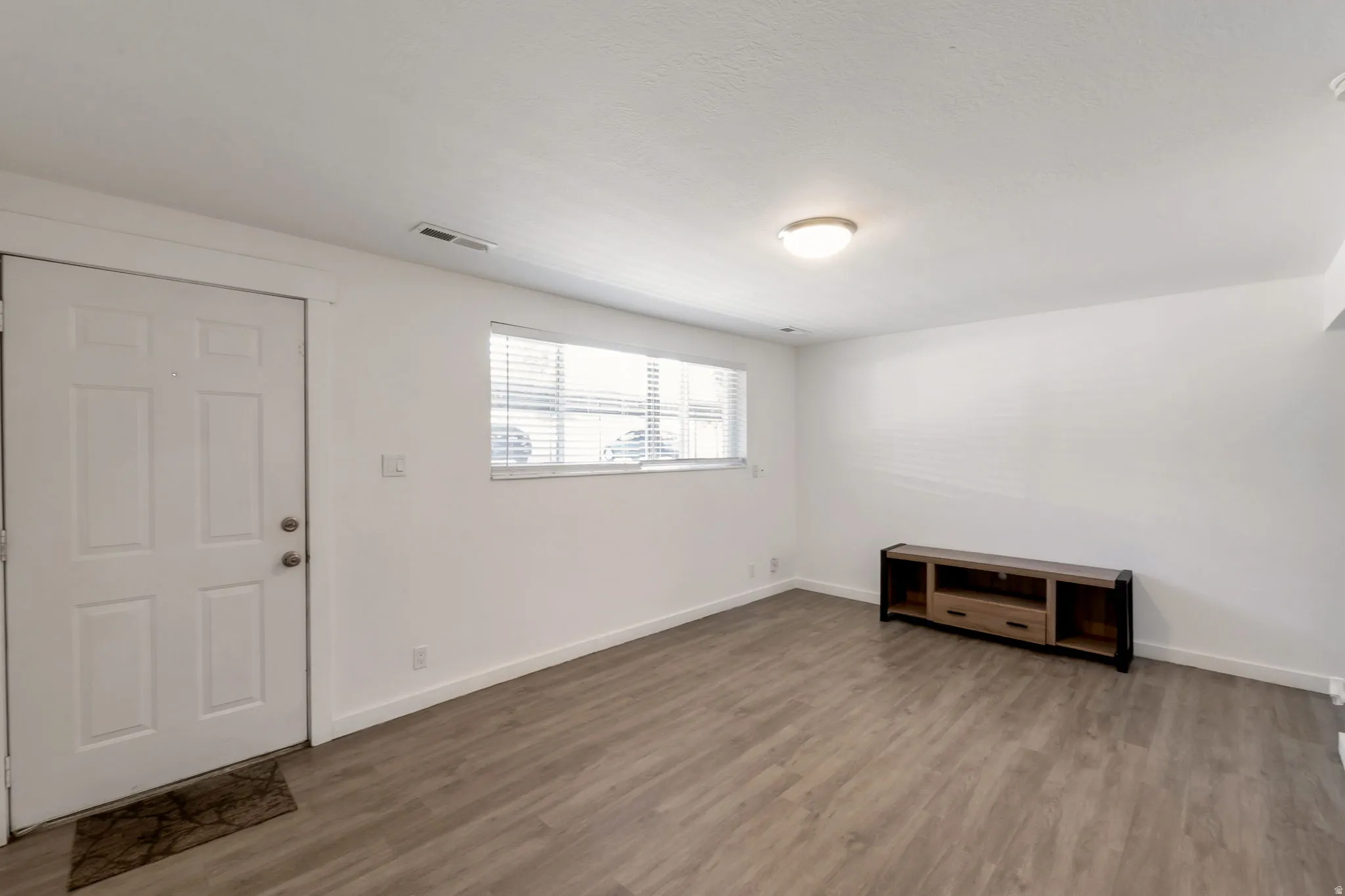 Spacious living area featuring wood-finish flooring, white baseboards, and a neutral color palette