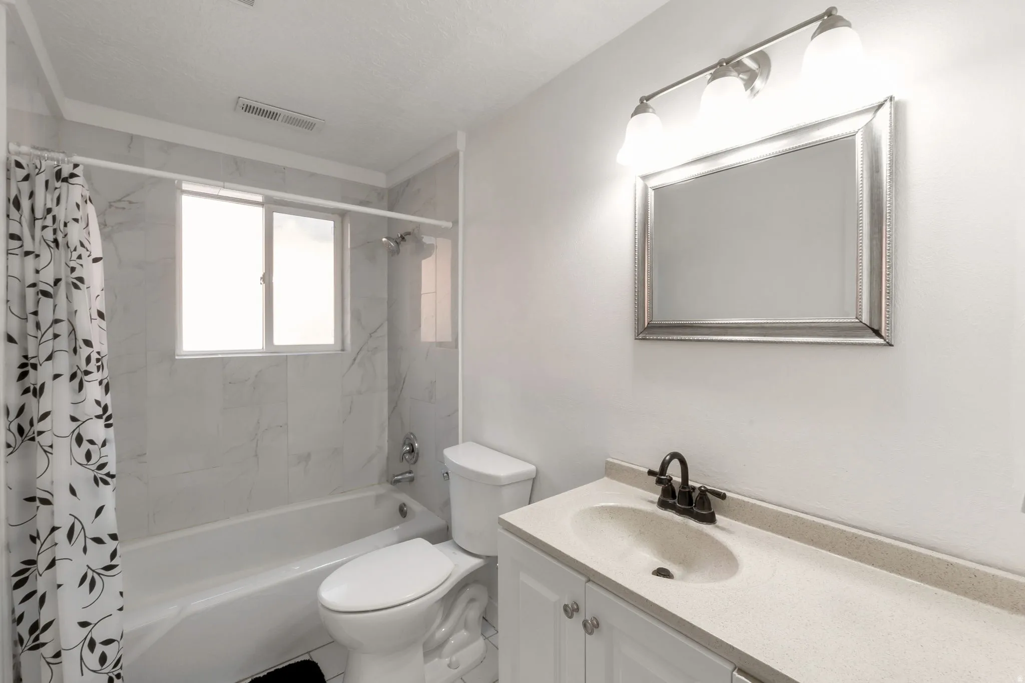 Bathroom featuring a tub/shower combination with white tile surround, a window, and a vanity with an integrated sink and dark bronze faucet