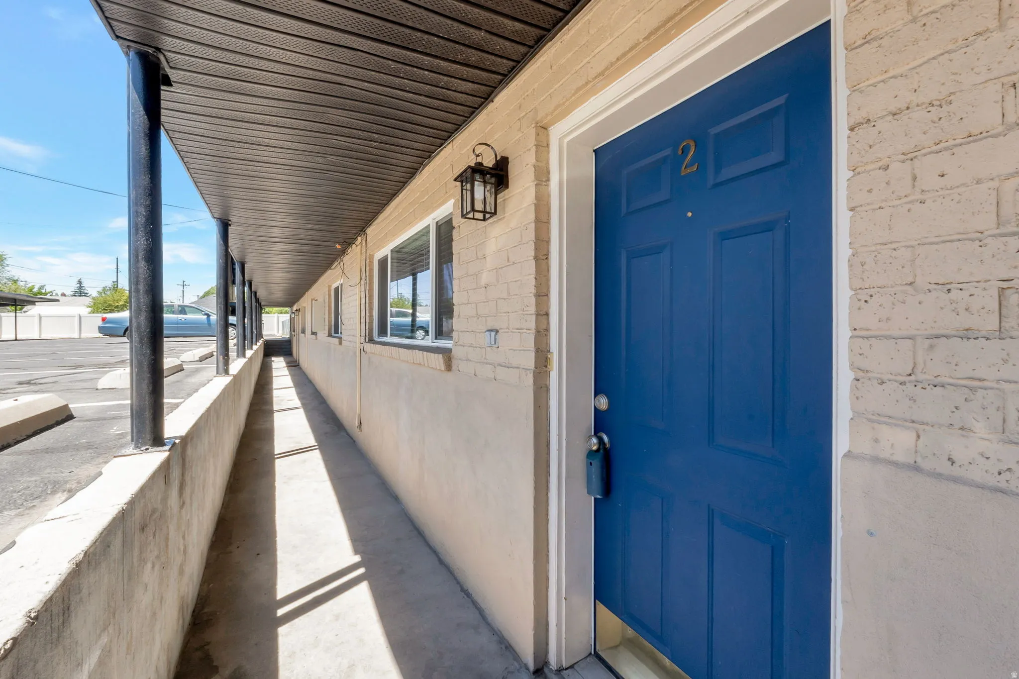 Entryway featuring a bright blue paneled door with gold-toned numbering, brick facade, and an exterior lantern sconce