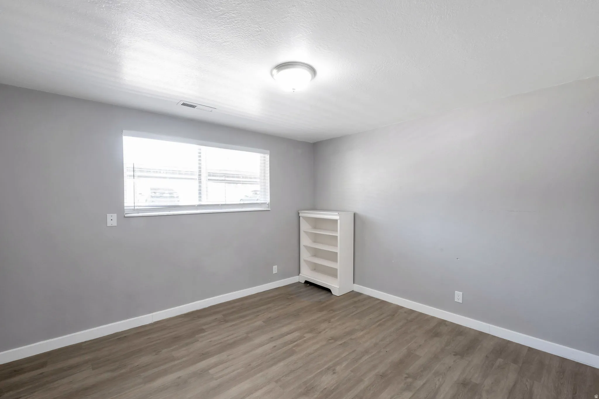 Room with wood-finish flooring, light gray wall paint, and white baseboards