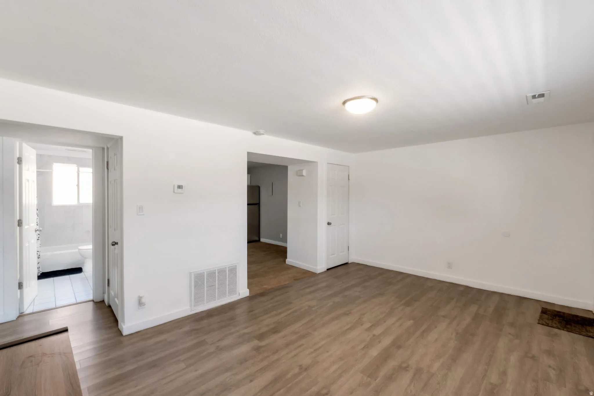 Spacious room with wood-finish flooring, white walls, and a ceiling-mounted light fixture