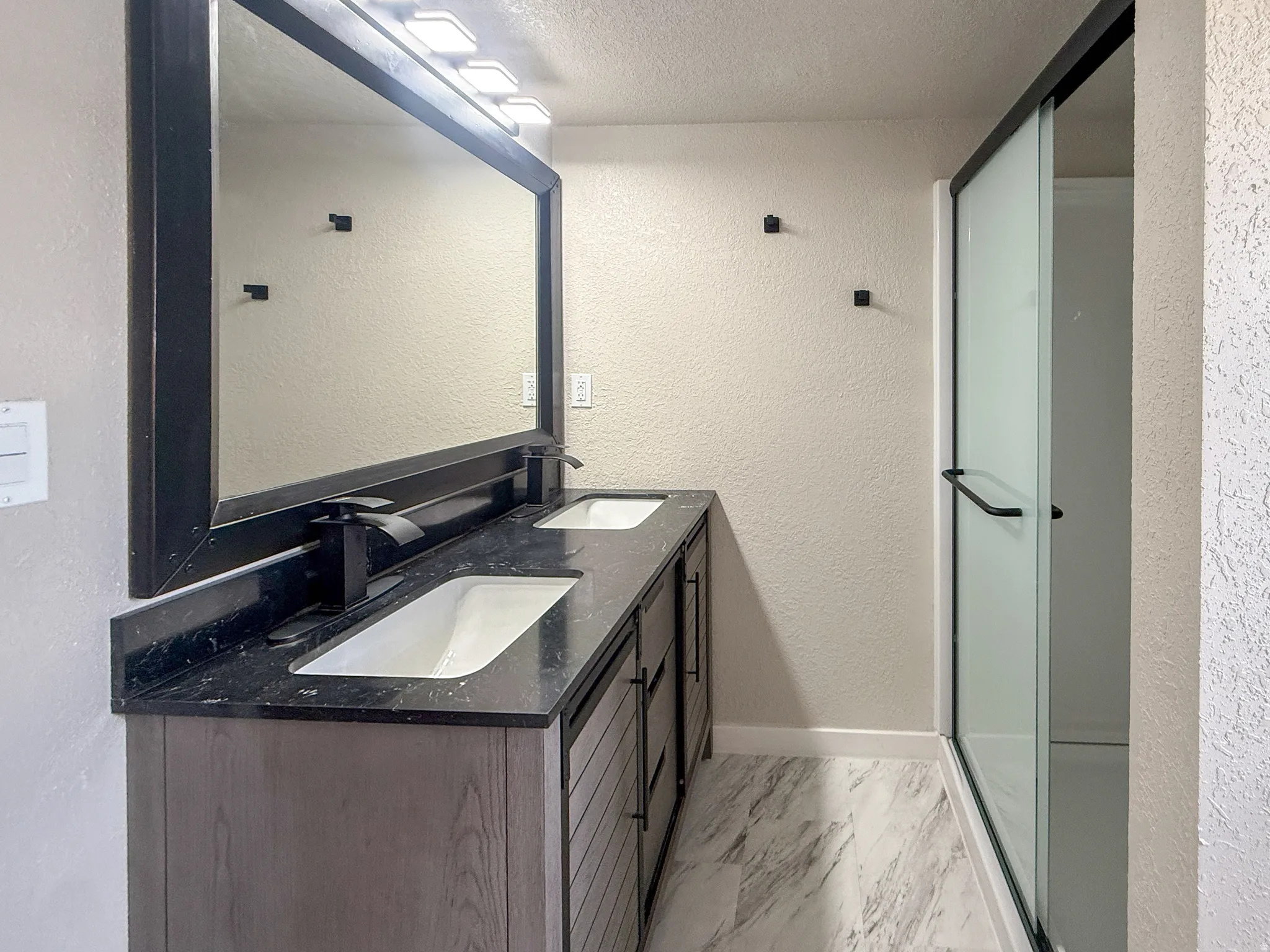 Modern bathroom featuring a dual vanity with a dark wood-finish cabinet and black countertop, dual undermount sinks, and black wall-mounted faucets