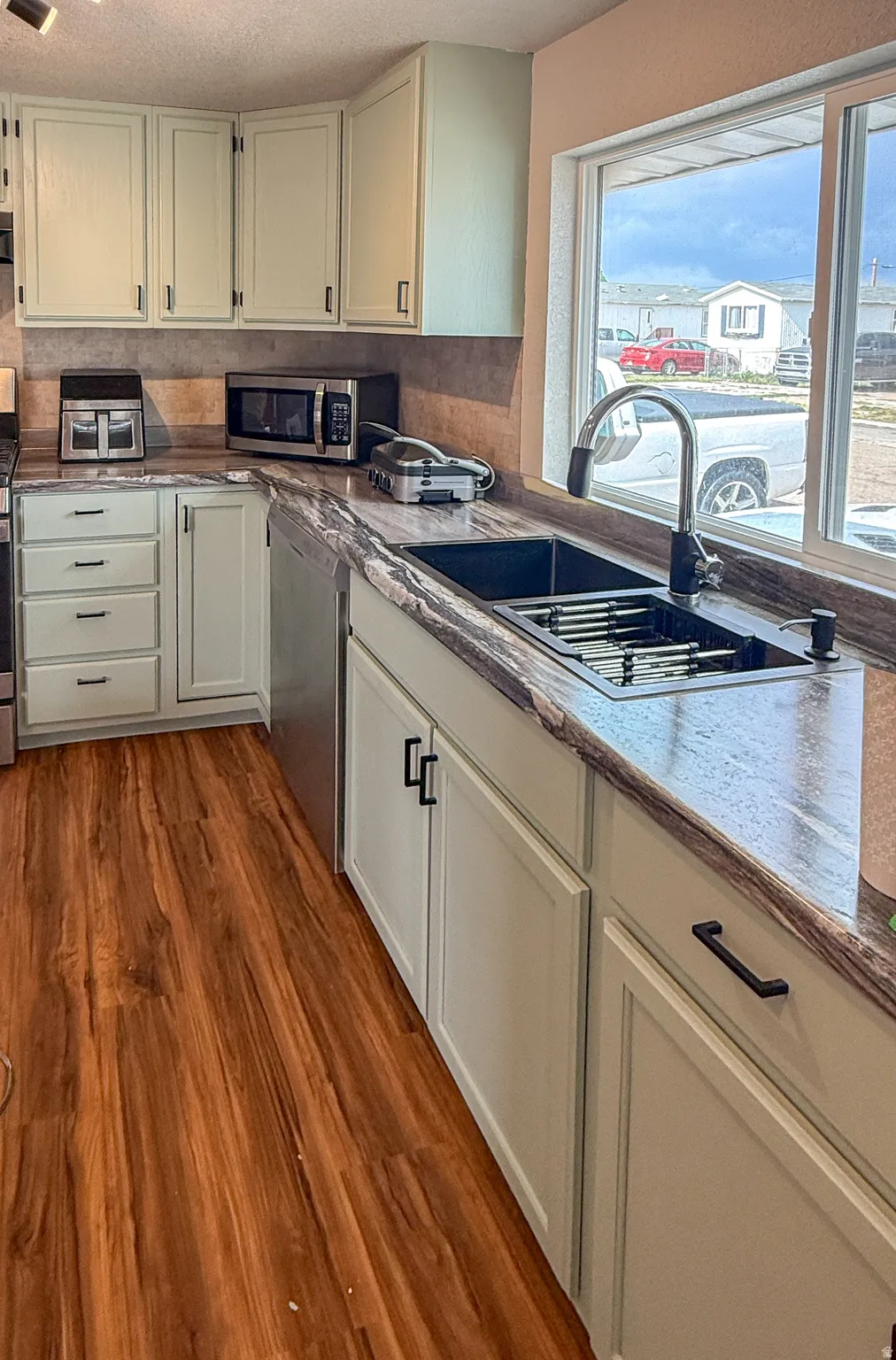 Kitchen featuring light-toned cabinetry, wood-finish flooring, dark countertops, a large window, and a black sink with a gooseneck faucet