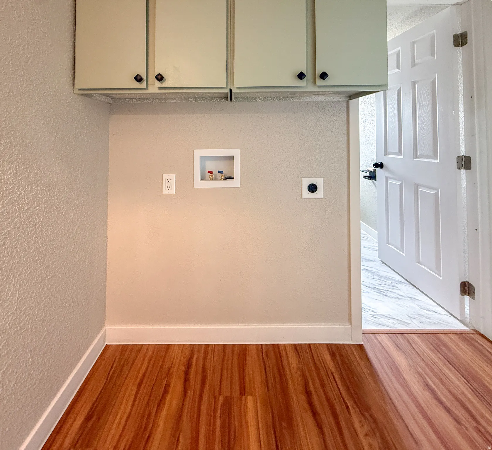 Dedicated utility area featuring wood-finish flooring and upper cabinetry with dark hardware