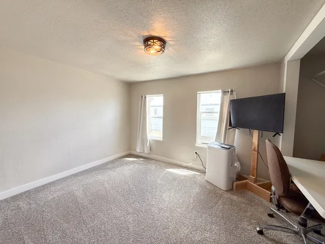 Spacious room featuring neutral-toned walls, textured ceiling, and gray carpeting