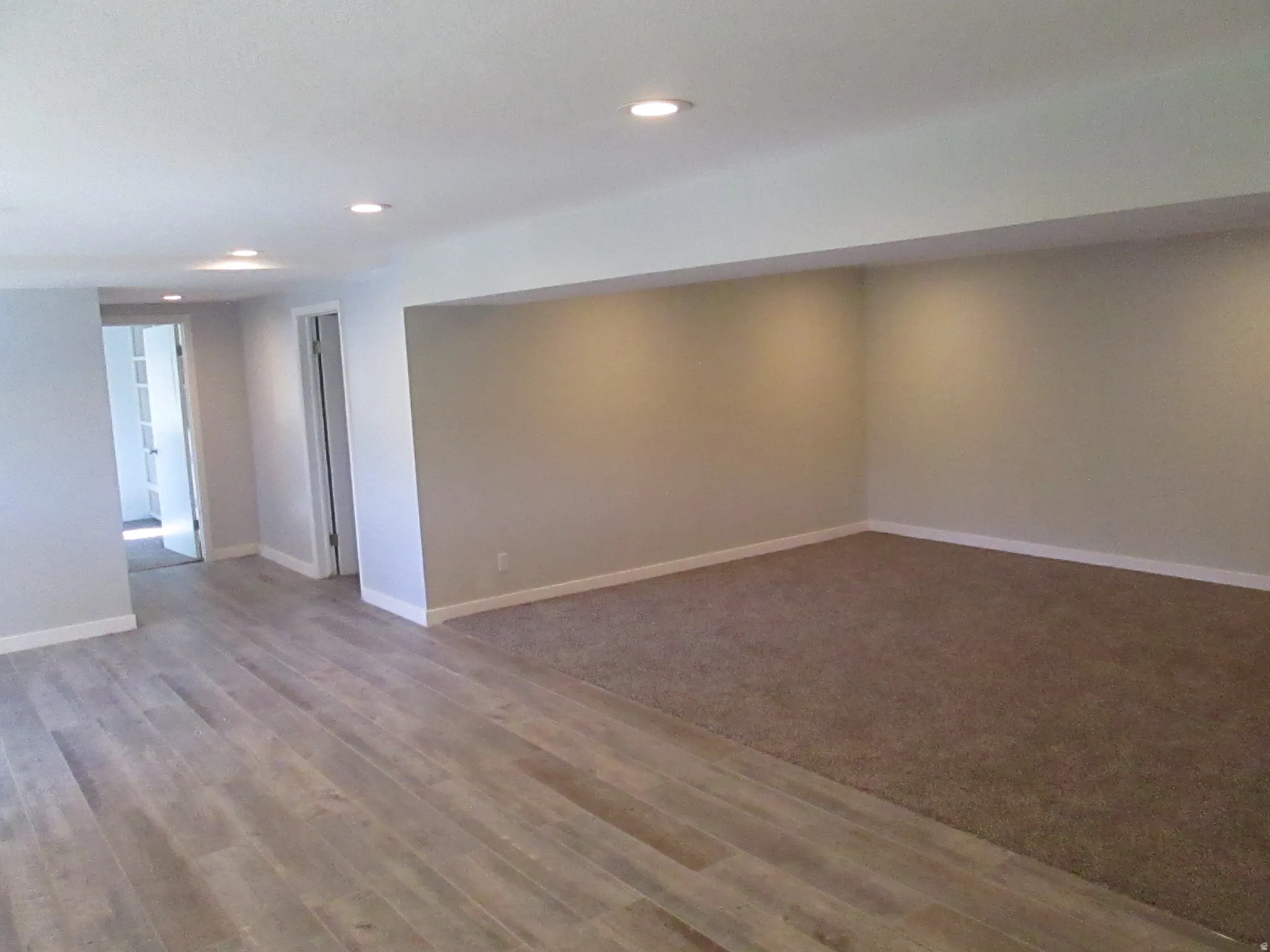 Spacious room featuring light wood-finish flooring, a plush carpeted area, recessed lighting, and neutral wall tones