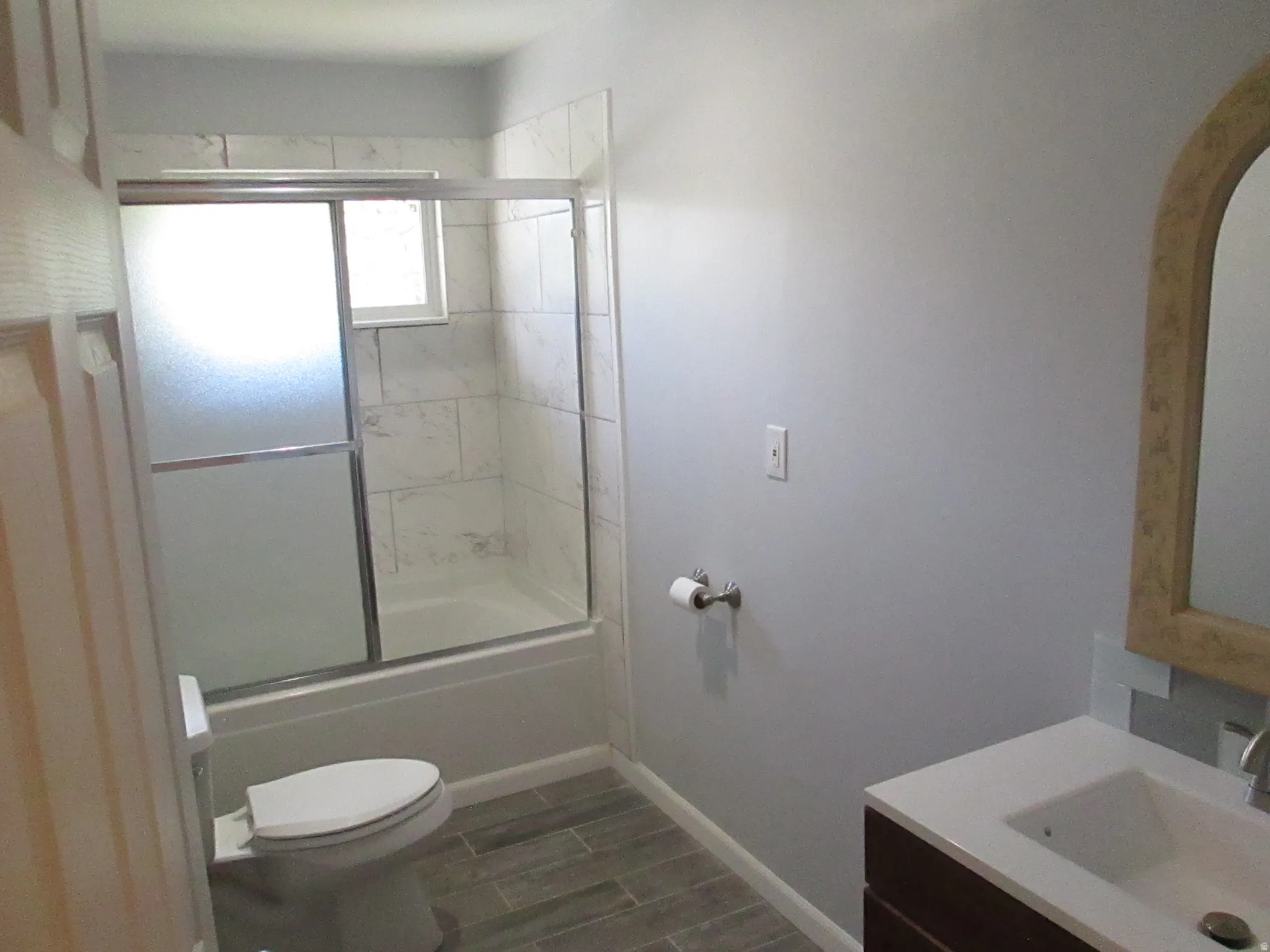 Bathroom featuring a full tub and shower with sliding glass doors, white tiled surround, modern vanity with an integrated sink, and wood-finish flooring