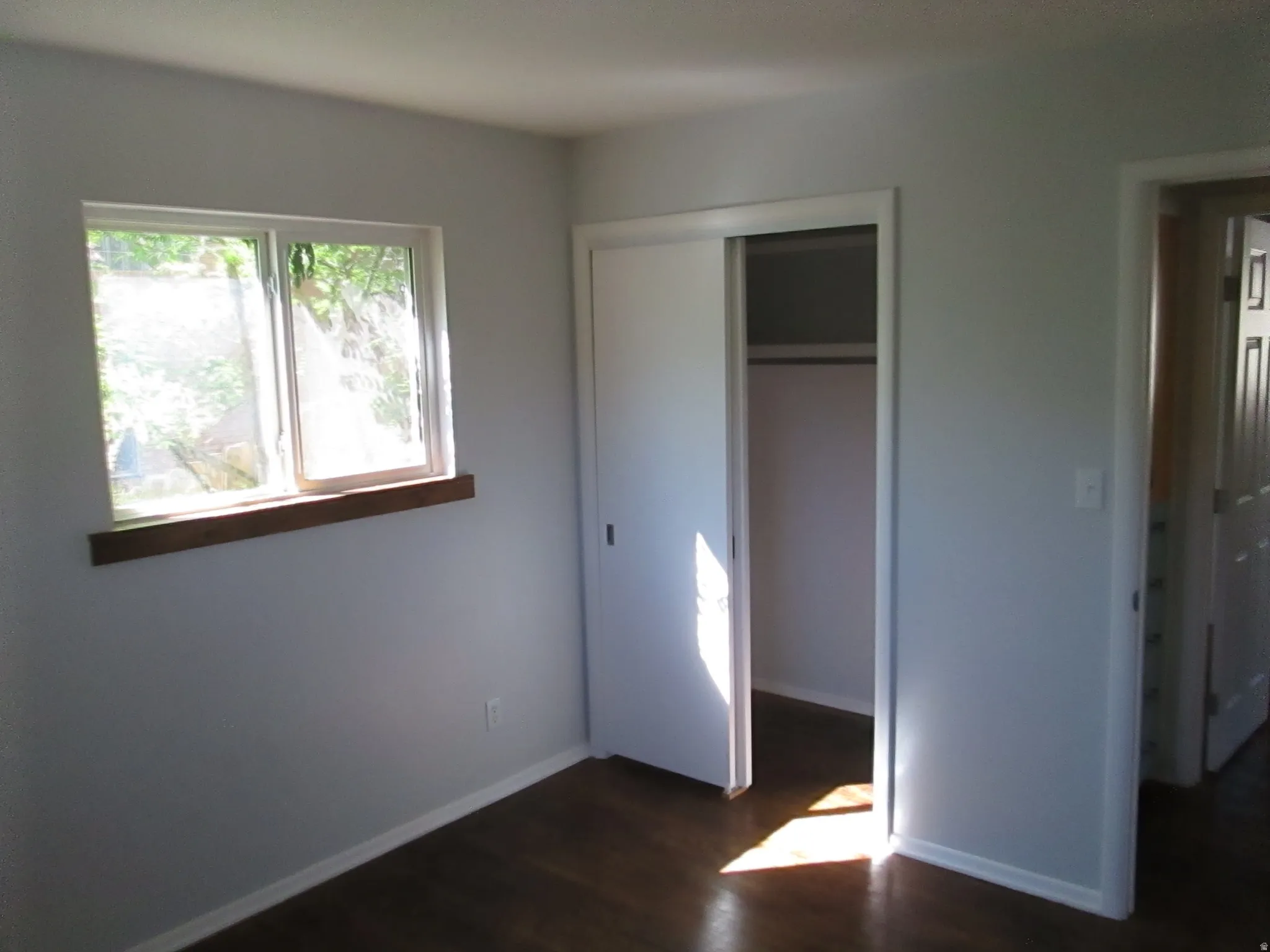 Room featuring wood-finish flooring, a double-paned window with a wood sill, and a closet with sliding doors