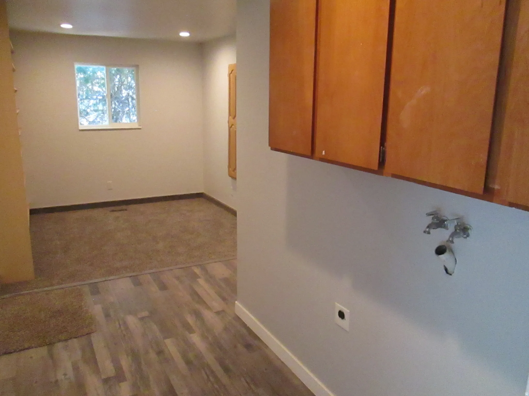 Kitchenette area featuring wood cabinetry, plumbing rough-ins for a washer and dryer, and wood-finish flooring