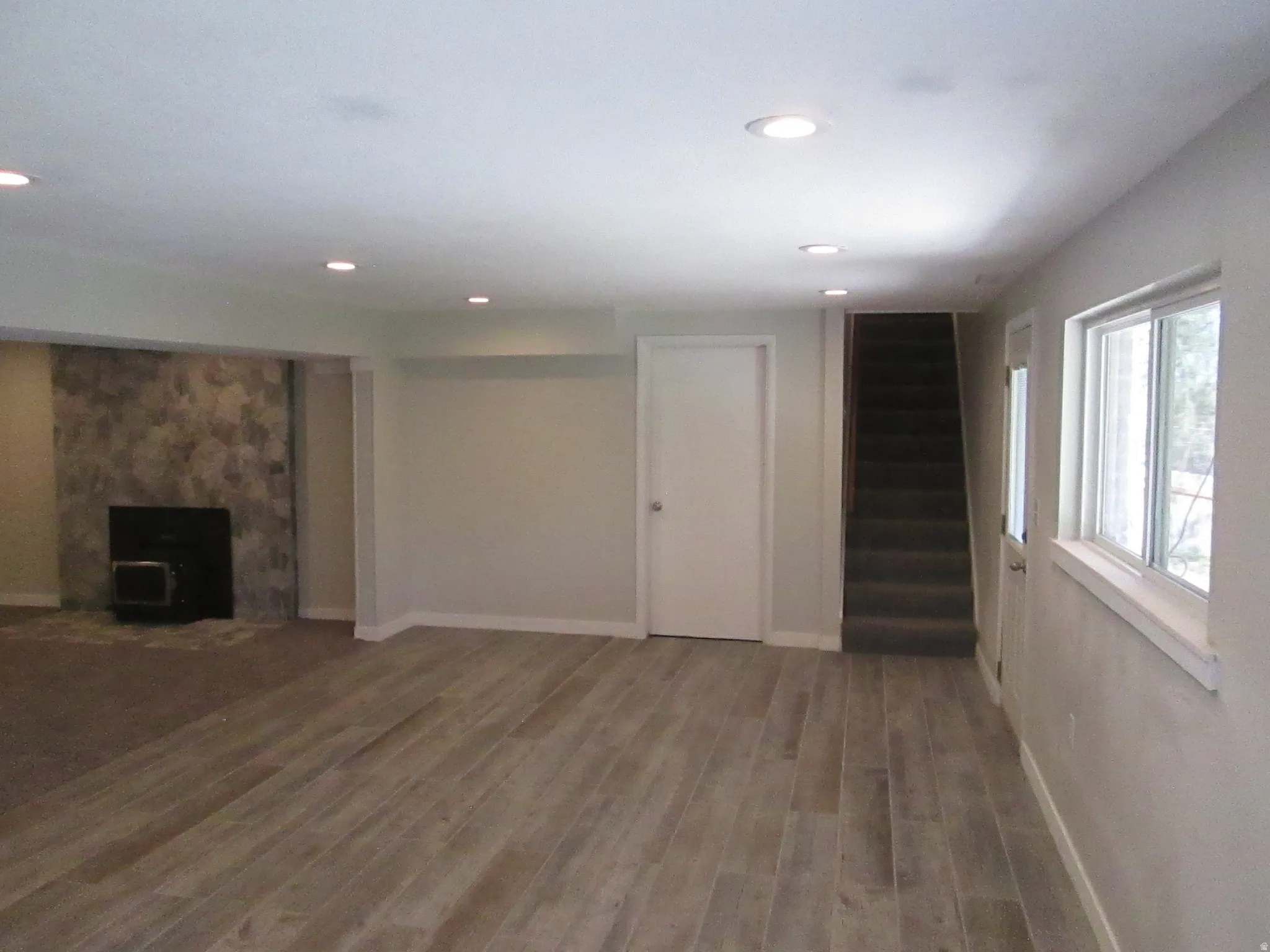 Spacious room featuring wood-finish flooring, recessed lighting, and a stone-clad fireplace with a dark hearth