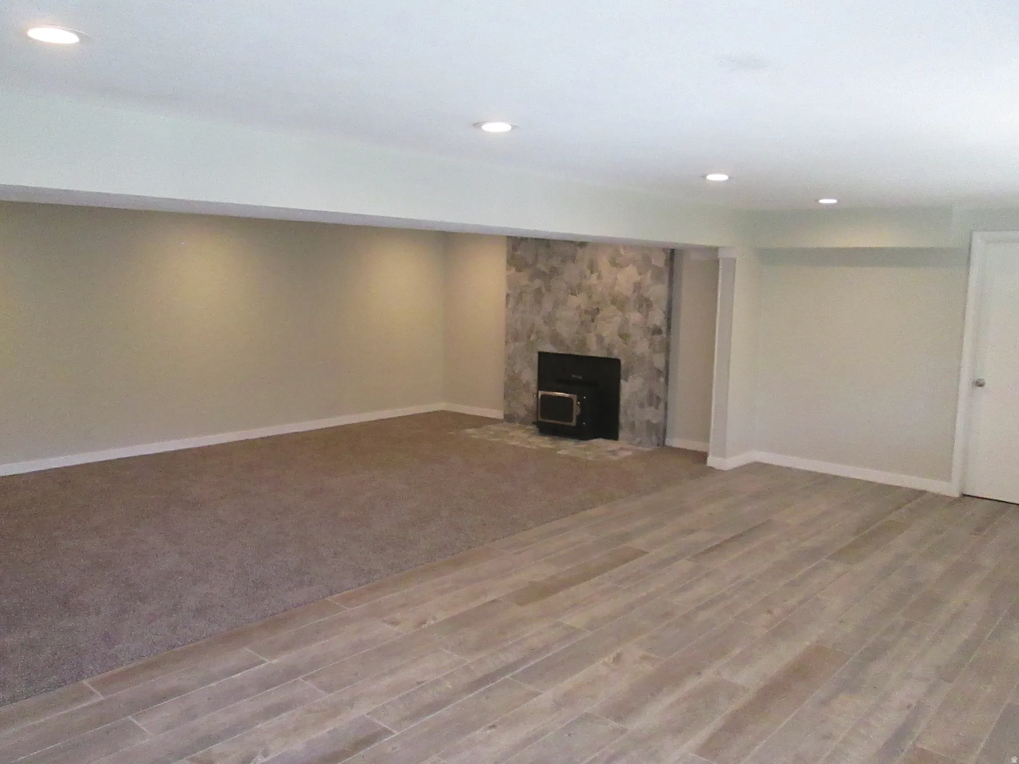 Spacious room featuring recessed lighting, a stone-clad fireplace with a dark insert, and a combination of wood-look flooring and carpeting