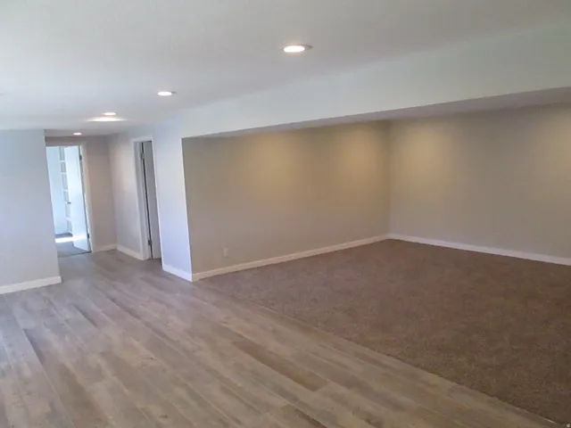 Spacious room featuring light wood-finish flooring, a plush carpeted area, recessed lighting, and neutral wall tones