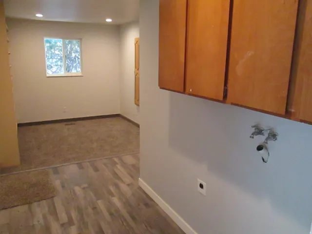 Kitchenette area featuring wood cabinetry, plumbing rough-ins for a washer and dryer, and wood-finish flooring