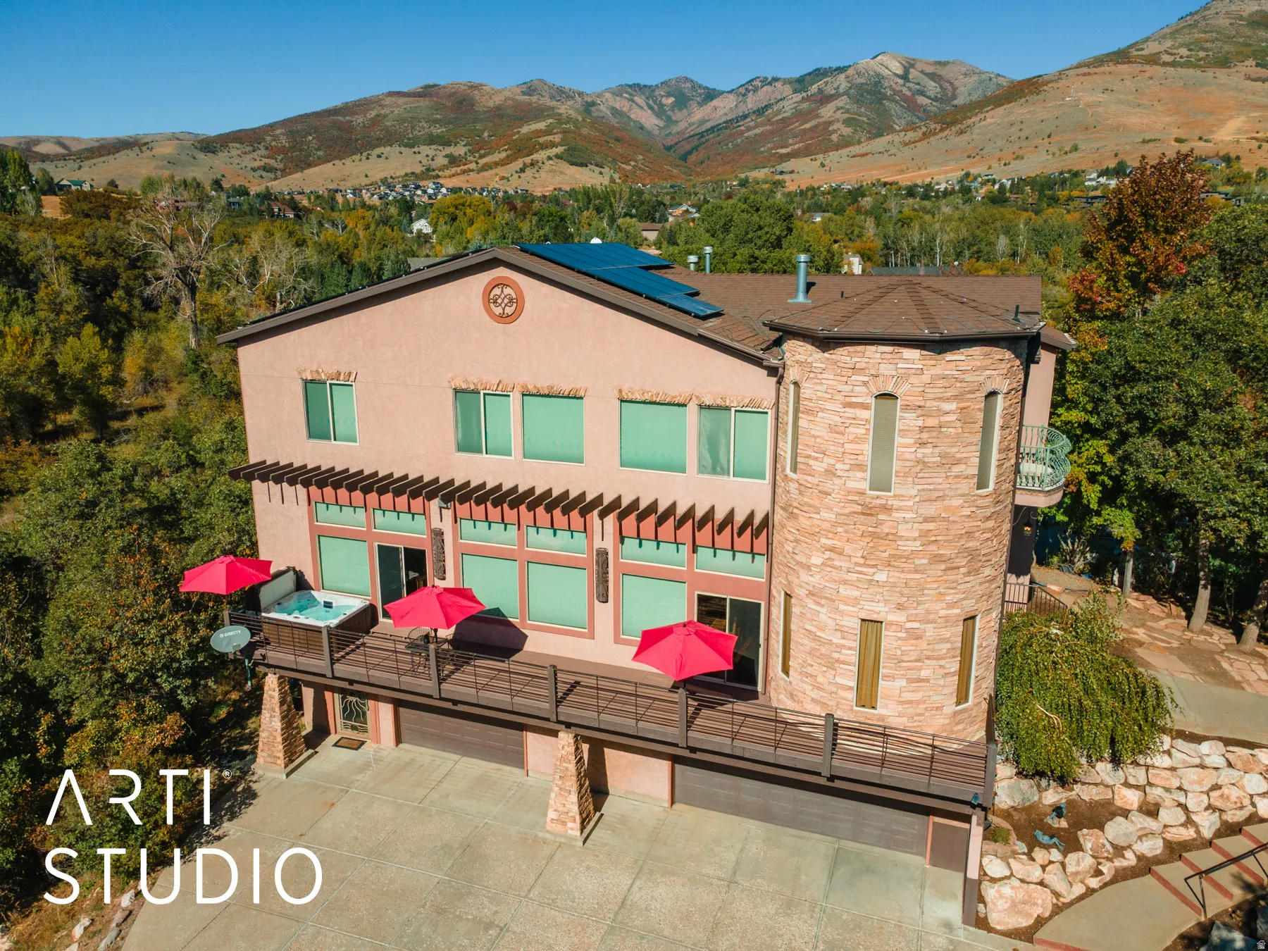 Multi-level stucco exterior featuring a prominent stone-clad turret, solar panels, and a full-width deck with a hot tub