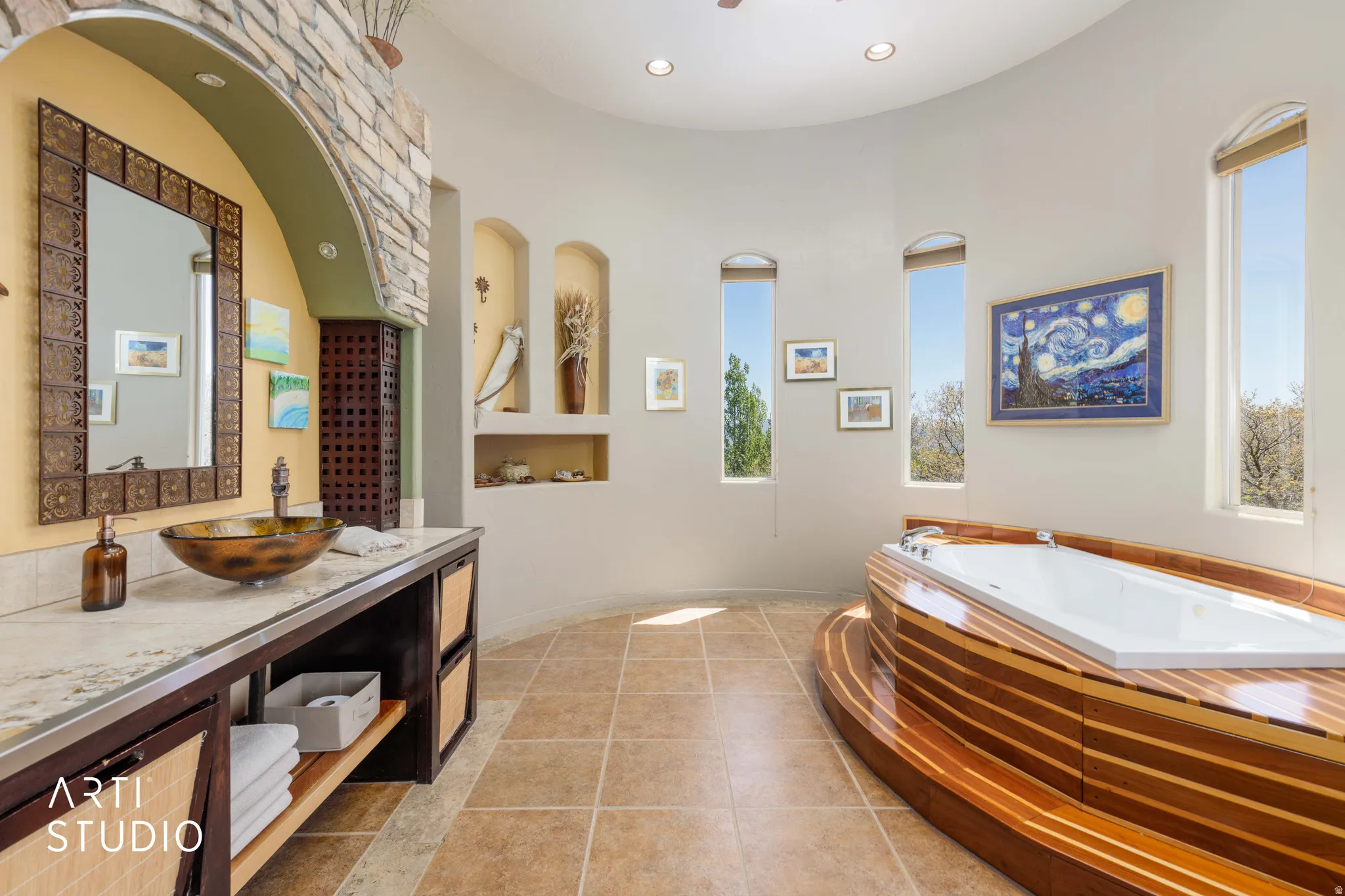 Curved wall bathroom featuring a built-in tub with wood-finish surround, multiple arched windows, and a vanity with a vessel sink and stone countertop