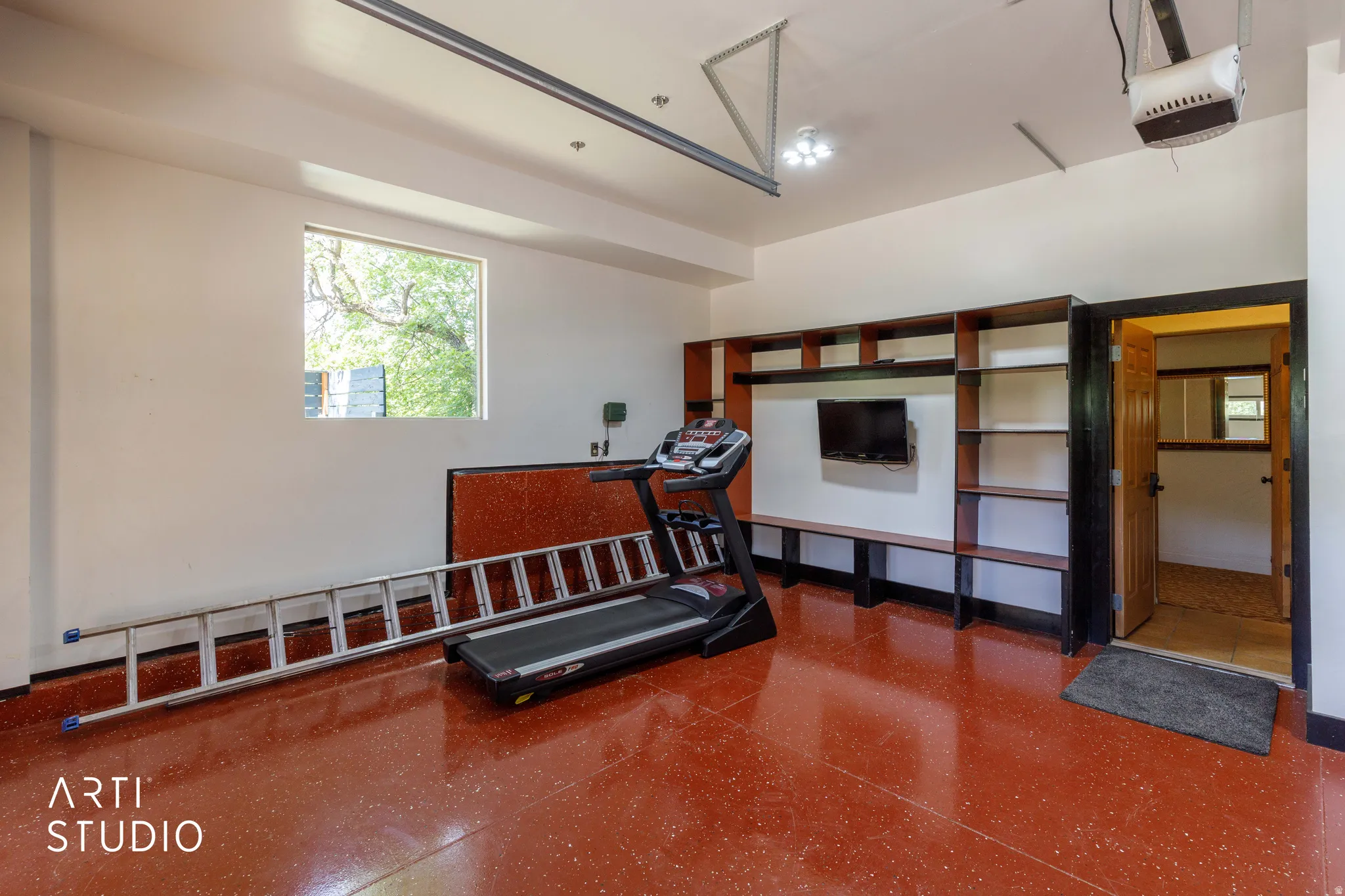 Garage space featuring a red-hued, textured floor and ample built-in shelving