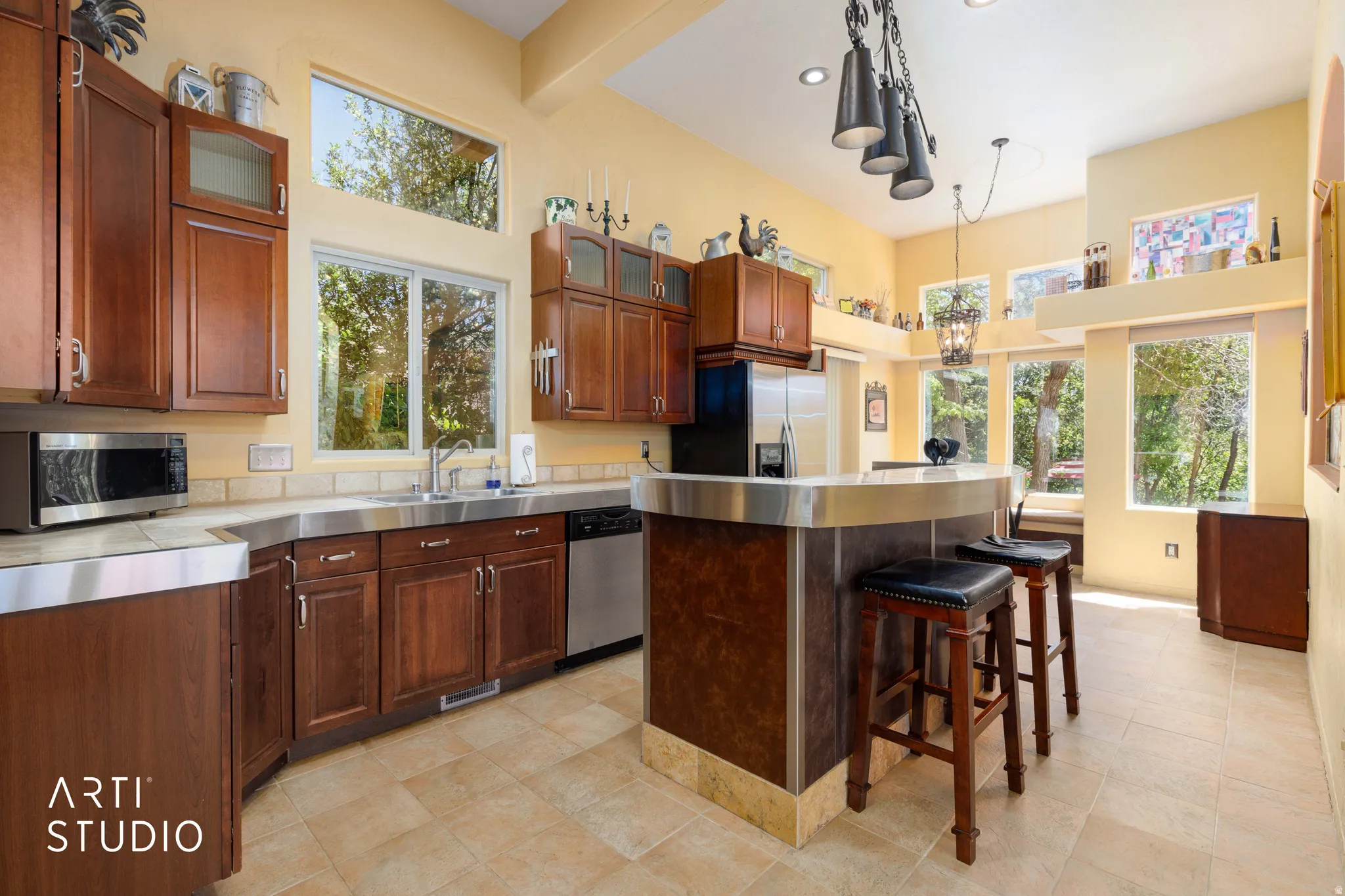 Kitchen featuring stainless steel countertops, wood cabinetry with glass-front accents, and a built-in breakfast bar