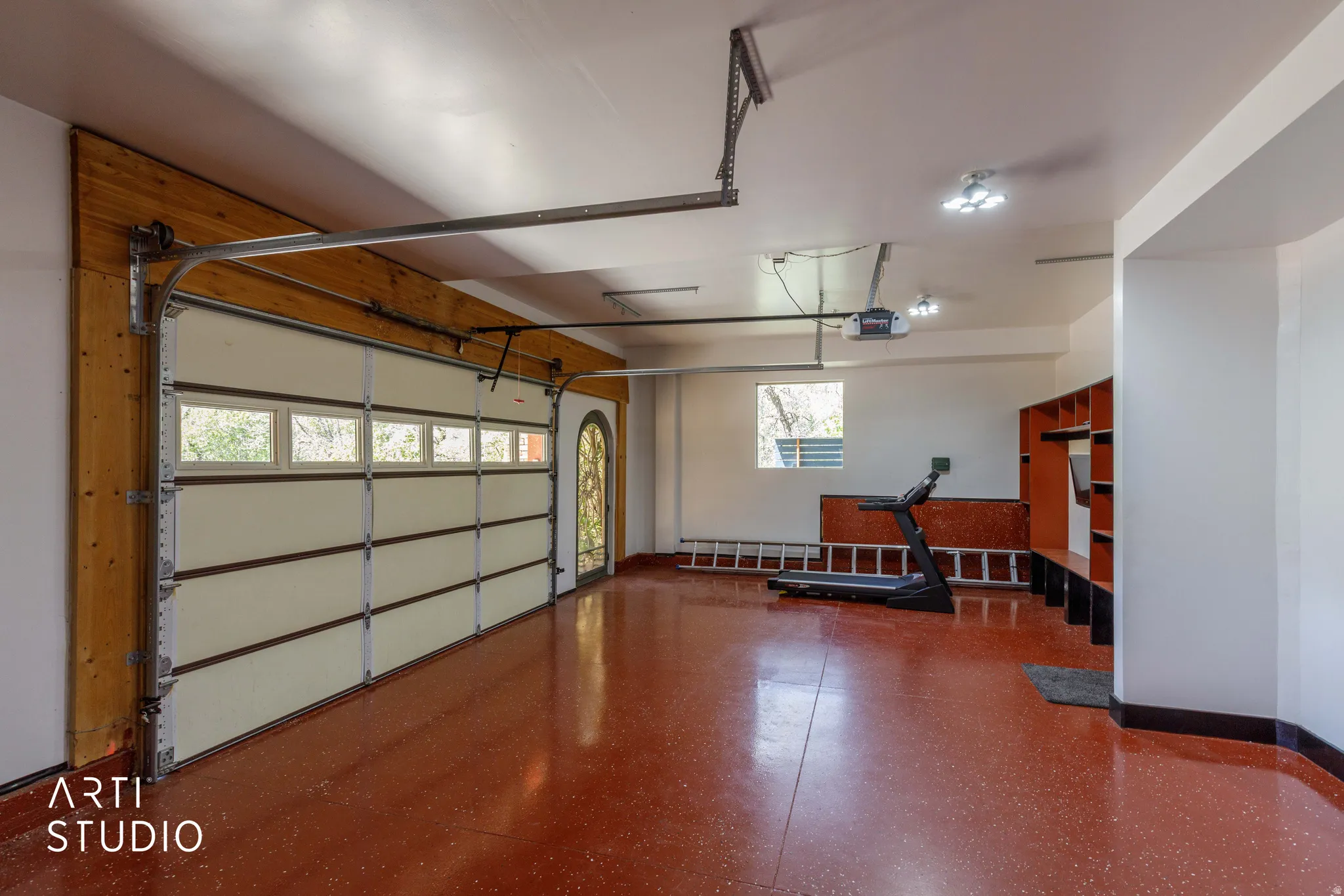 Spacious garage featuring a red epoxy floor, an overhead garage door with integrated windows, and an arched entry door