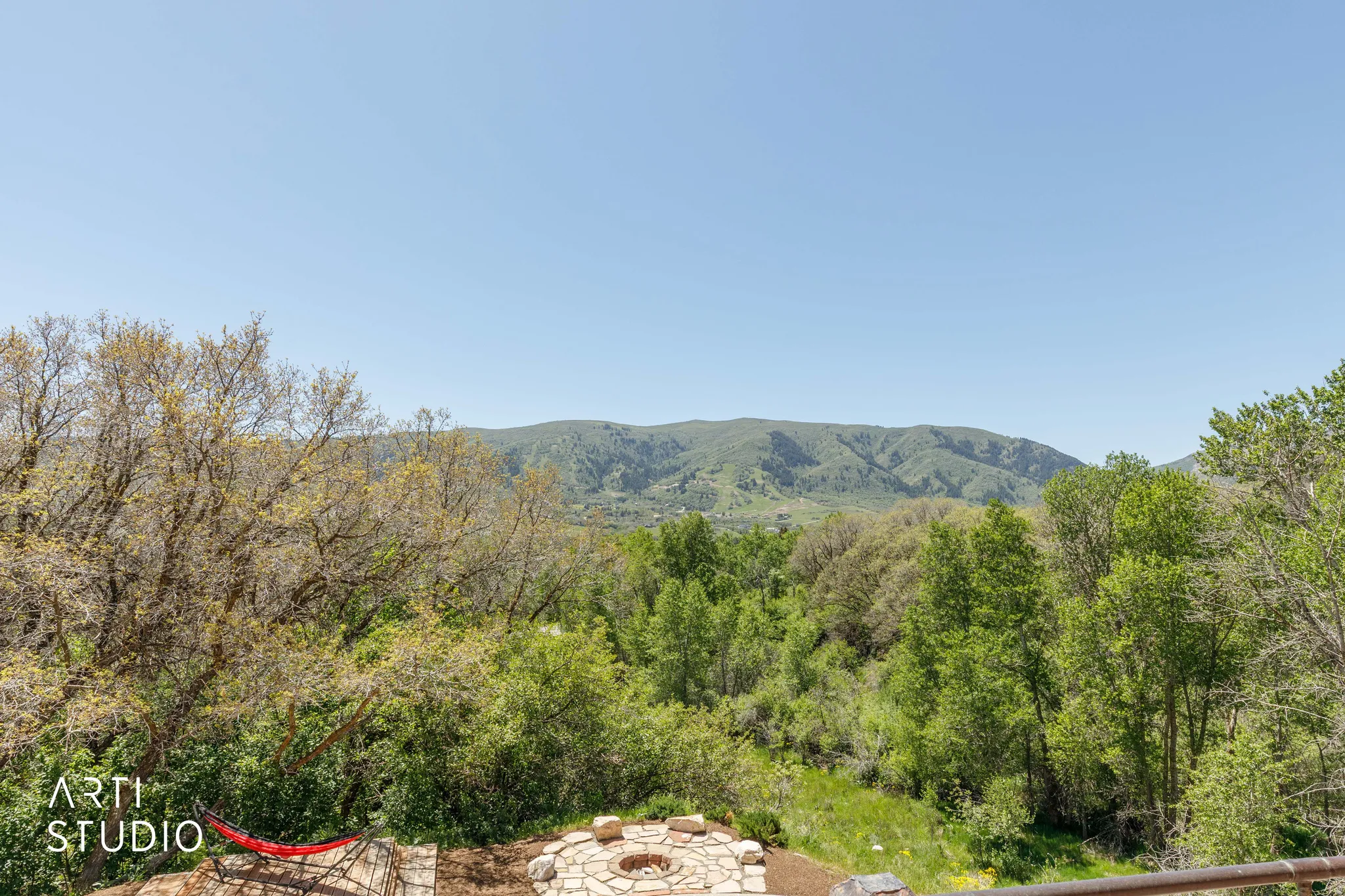 Outdoor fire pit area with stone surround, complemented by a surrounding natural landscape with abundant greenery and distant mountains