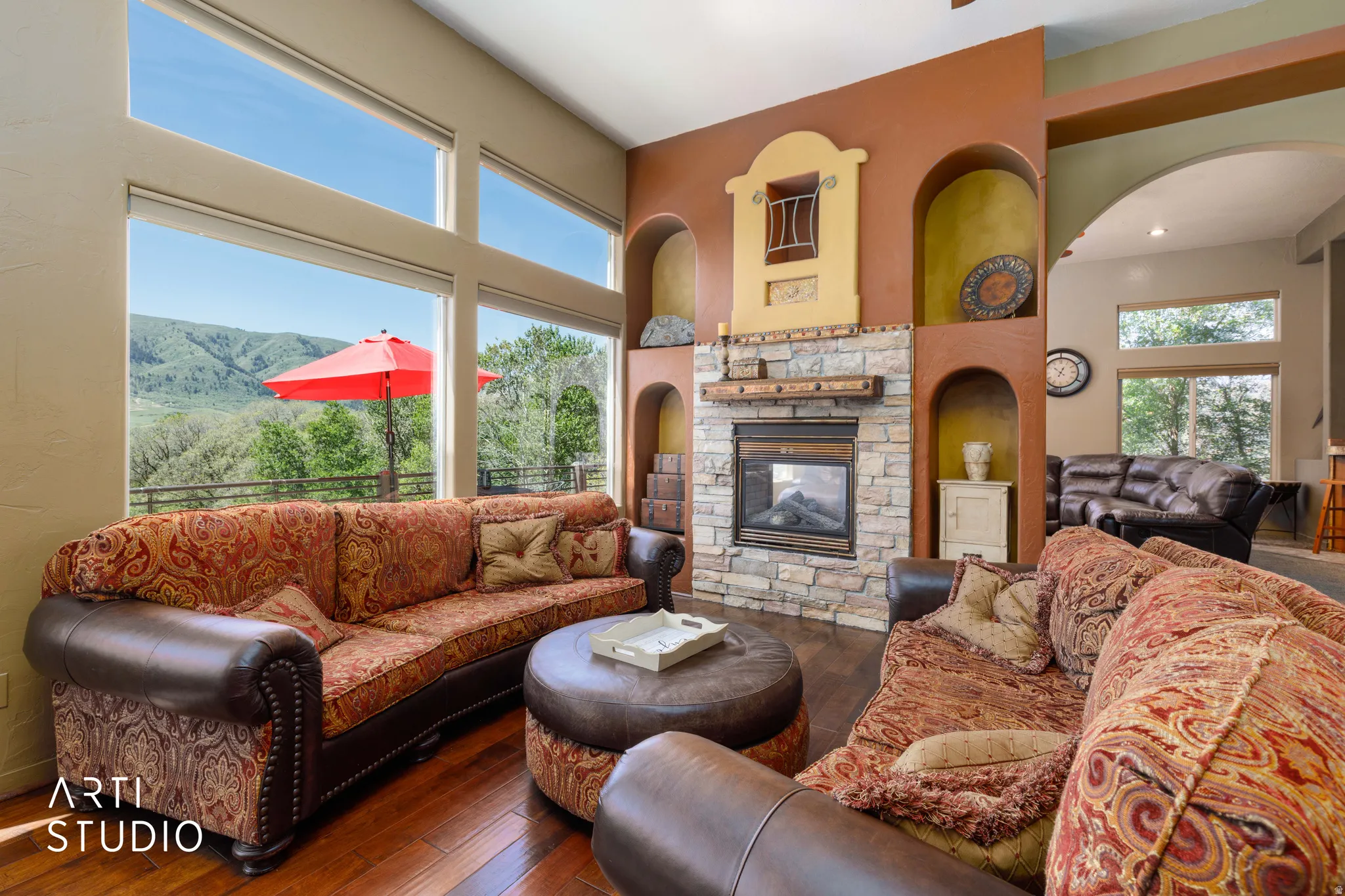 Expansive living area featuring a stone-clad fireplace with wood mantle, multiple arched display niches, and large windows with mountain scenery
