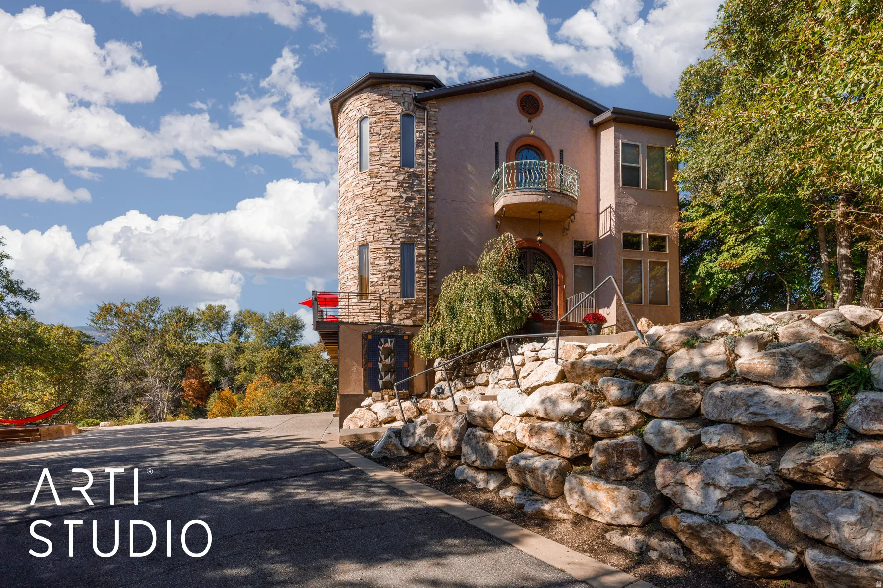 Multi-level stucco residence featuring a stone-clad turret, arched entry, and decorative wrought iron balcony