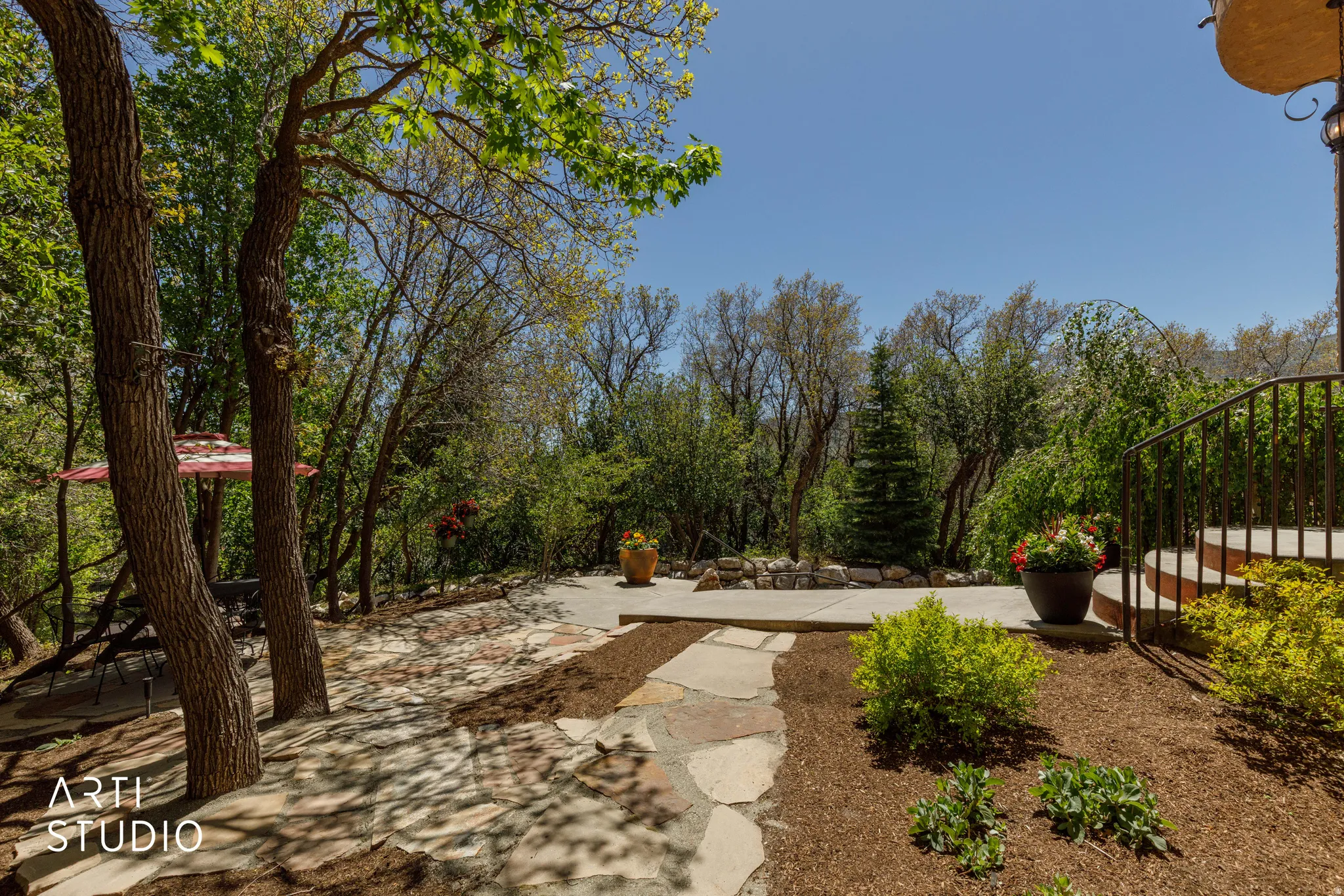 Flagstone patio with a stone retaining wall, surrounded by mature trees and lush landscaping