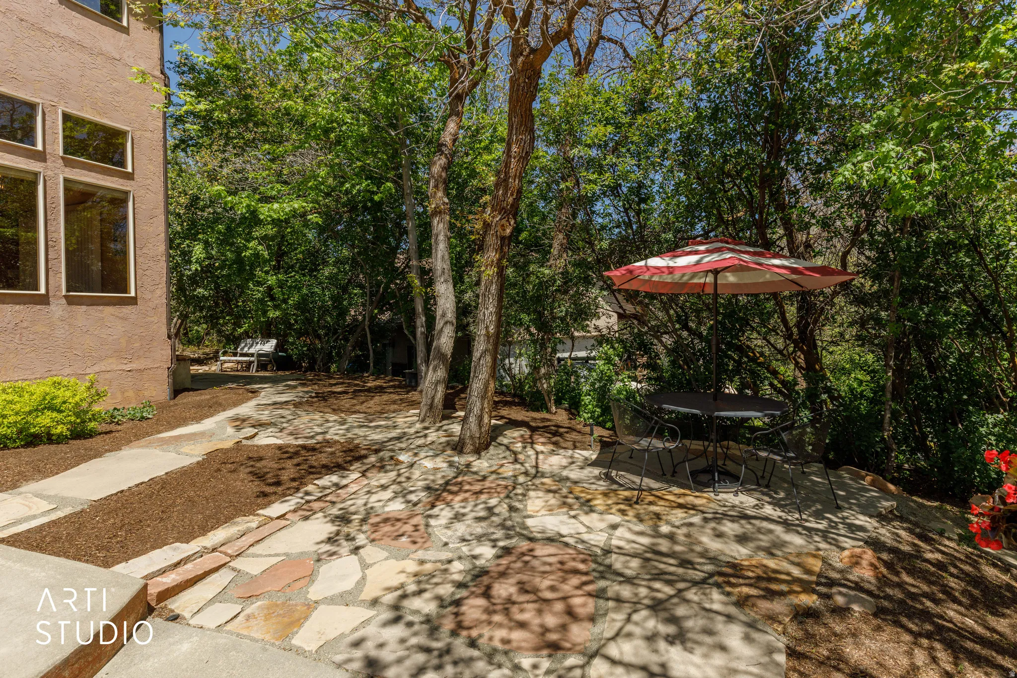Landscaped outdoor area featuring a flagstone patio, mature trees, mulch ground cover, and a stone pathway