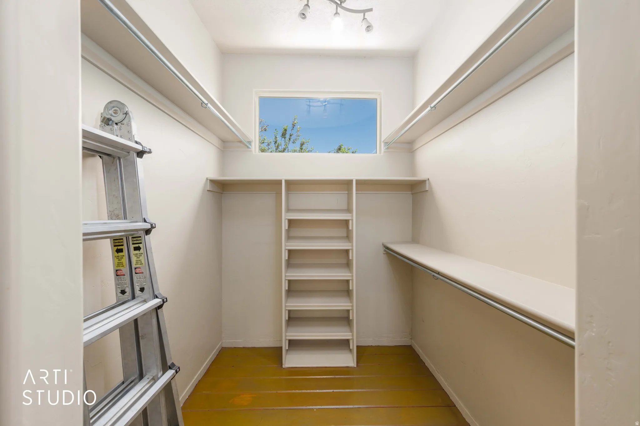Walk-in closet featuring built-in shelving, hanging rods, an upper window, and track lighting
