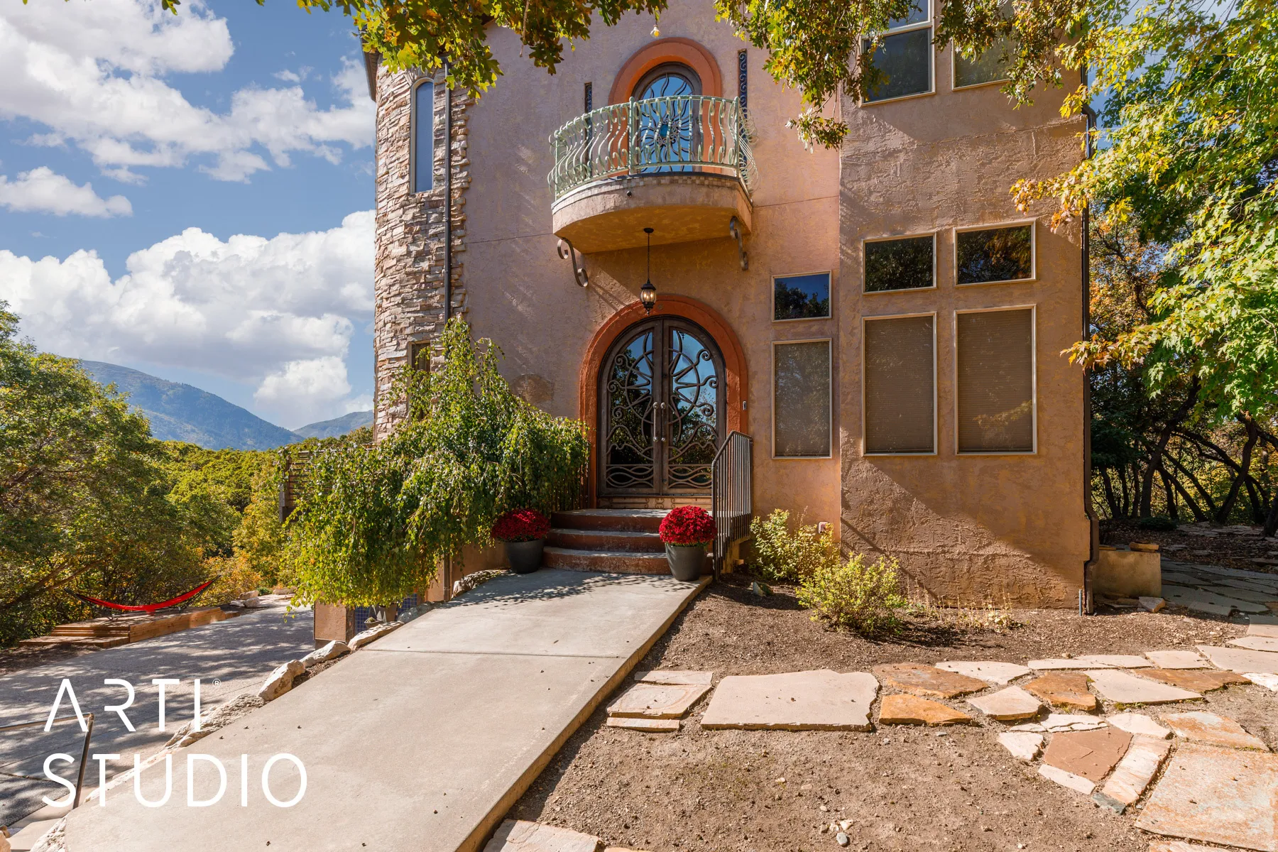 Stucco exterior featuring a stone accent tower, ornate double entry doors, a curved balcony with decorative ironwork, and a concrete walkway with flagstone detailing