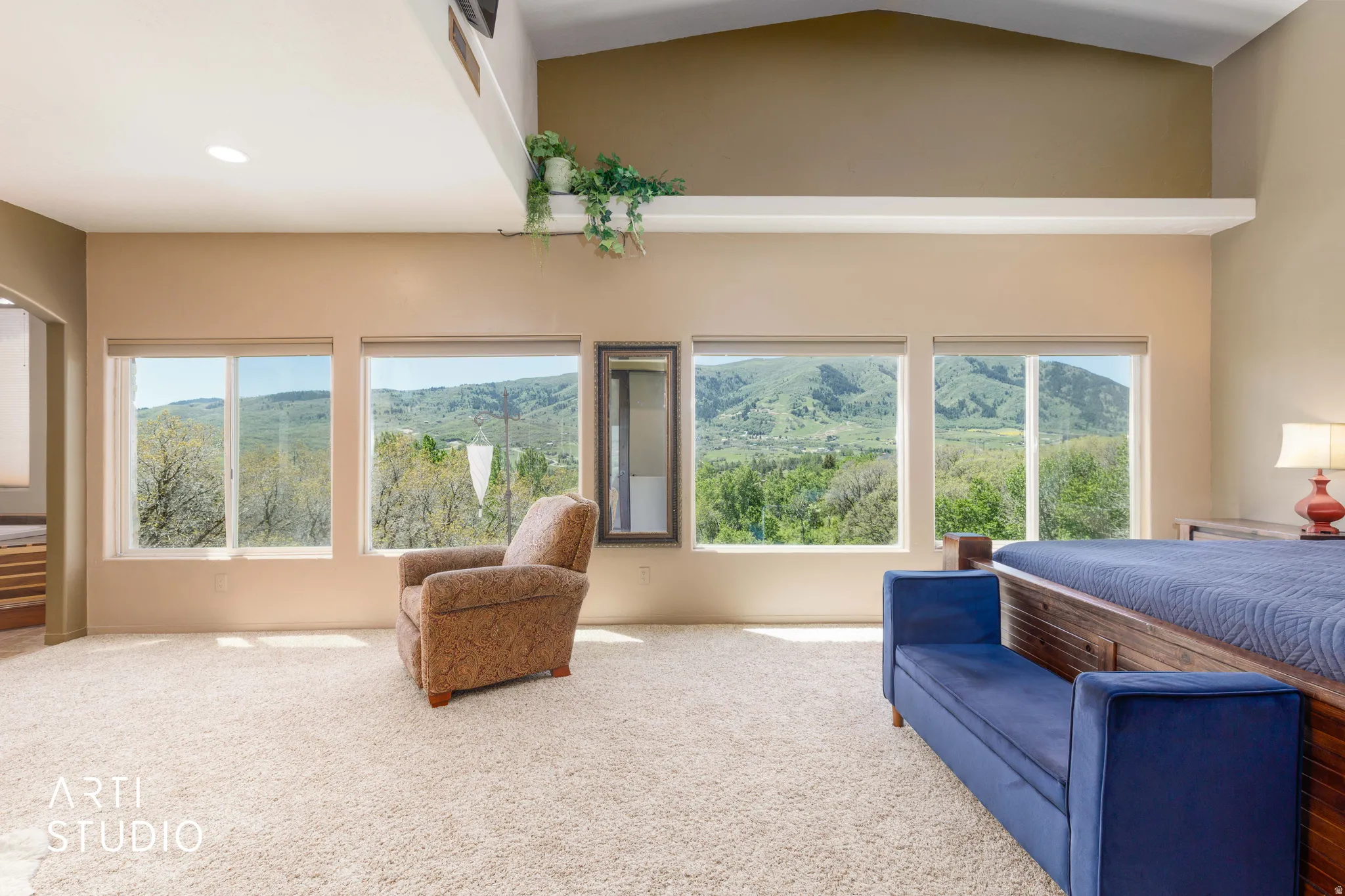 Spacious room featuring vaulted ceilings, a decorative ledge, recessed lighting, and expansive windows offering a scenic mountain and tree-filled landscape