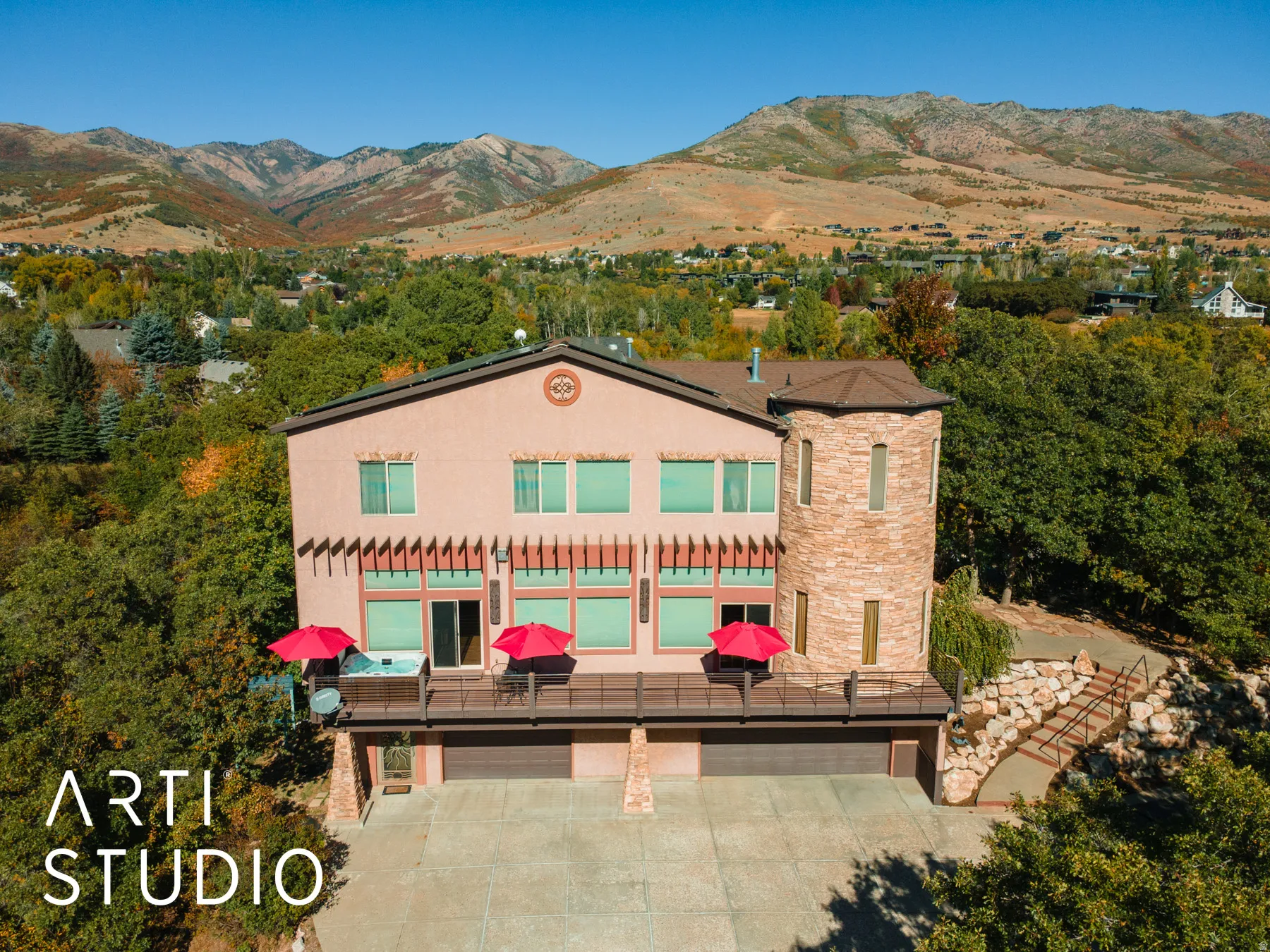 Stucco exterior with stone turret architectural feature, multi-level deck, attached two-car garage, and a concrete driveway