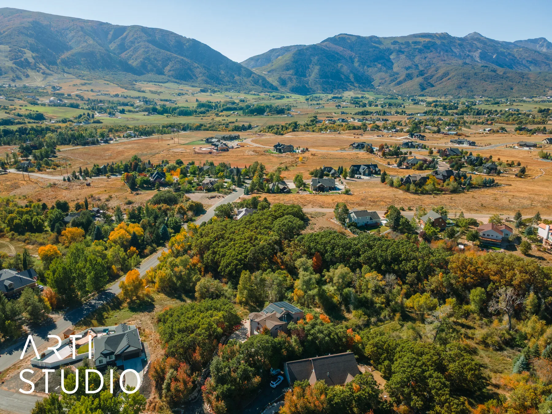 Expansive mountain landscape featuring a valley with residential properties, natural foliage, and distant peaks