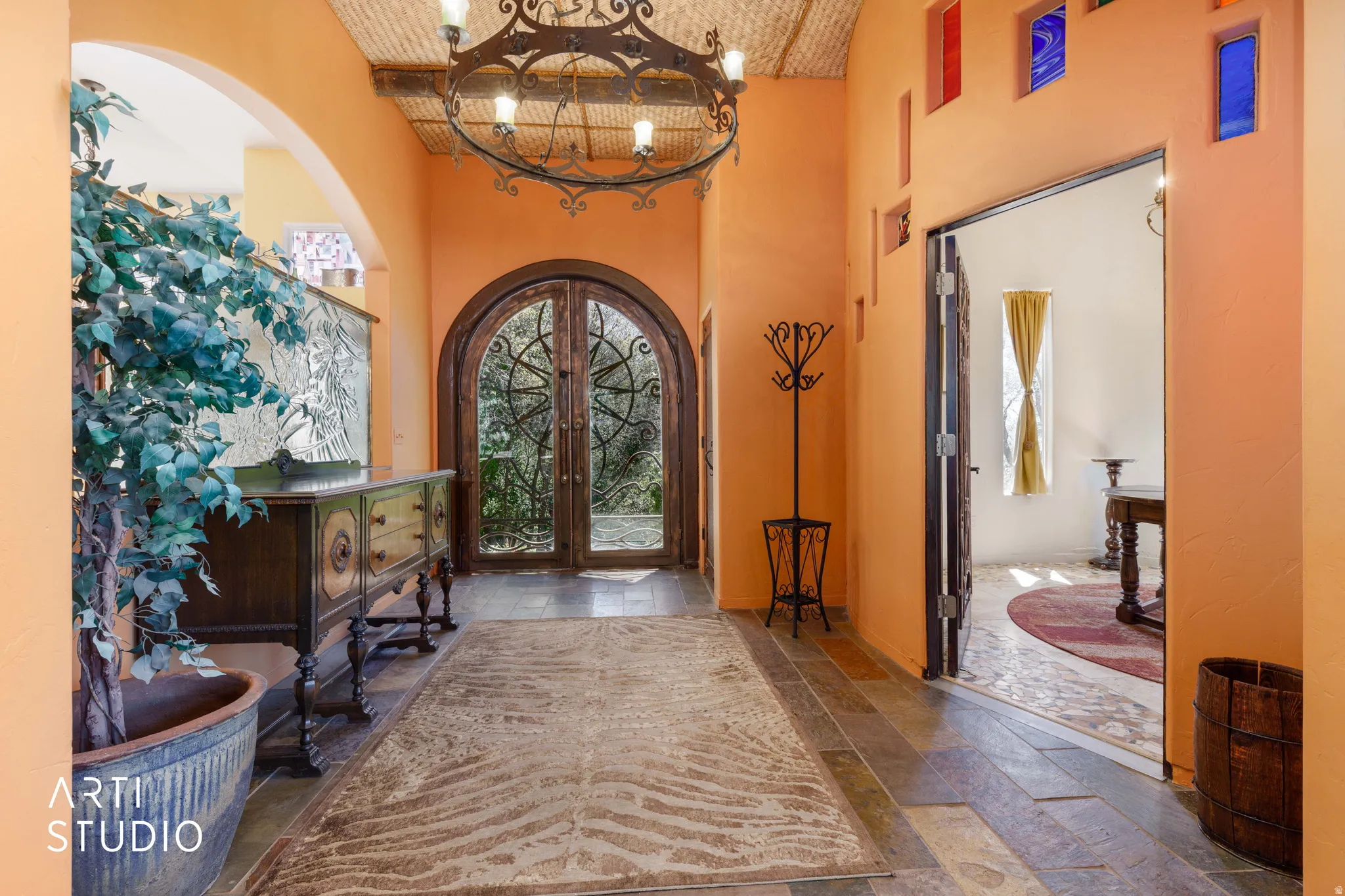 Arched double-door entryway with intricate ironwork and an overhead wrought iron chandelier