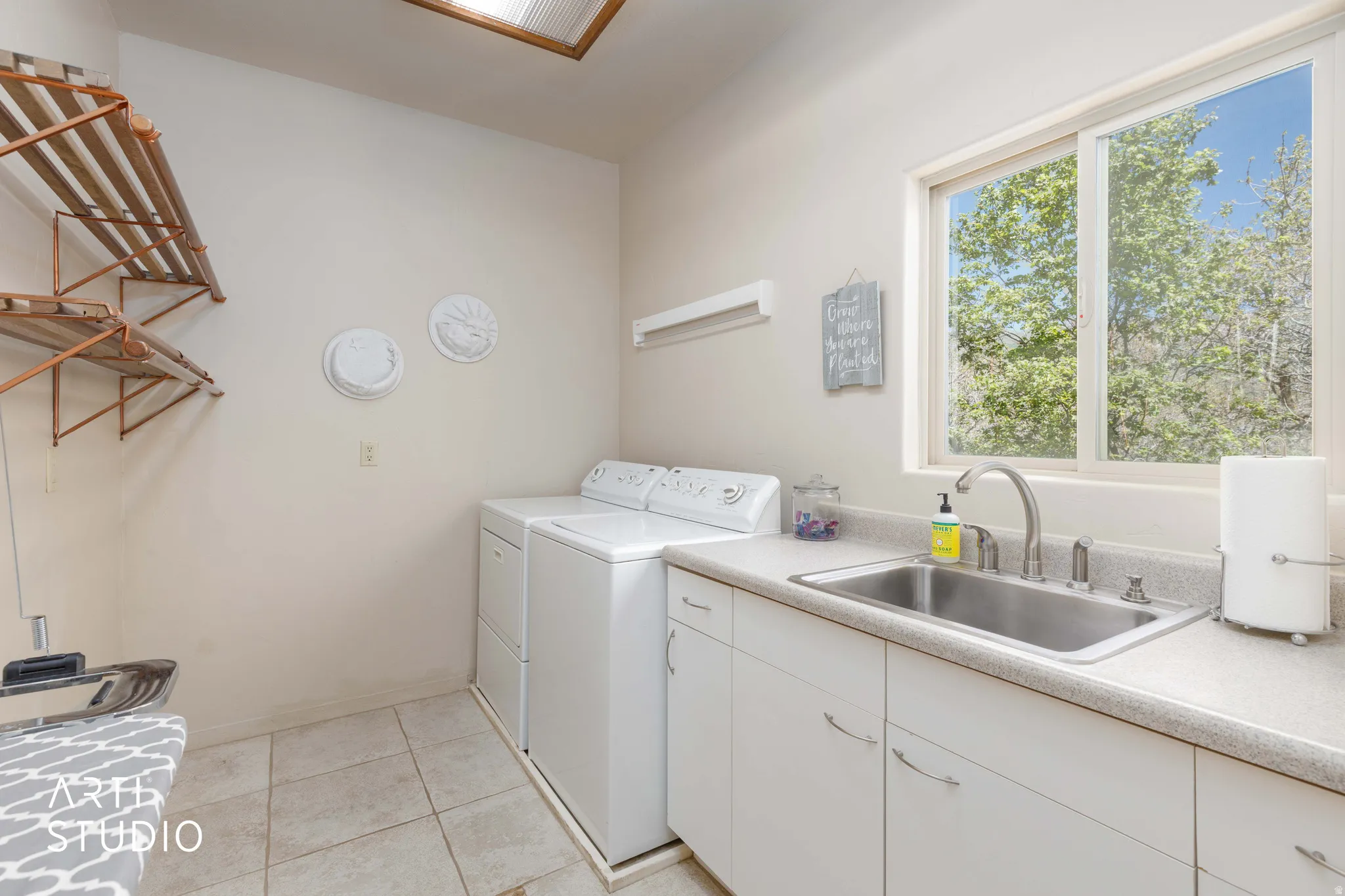 Utility room featuring a large window, a stainless steel sink, white cabinetry, and tile flooring