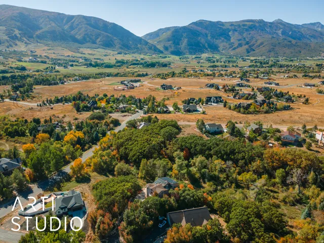 Expansive mountain landscape featuring a valley with residential properties, natural foliage, and distant peaks