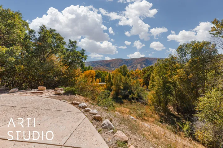 Expansive concrete patio area with natural stone accents, surrounded by mature trees showcasing seasonal foliage