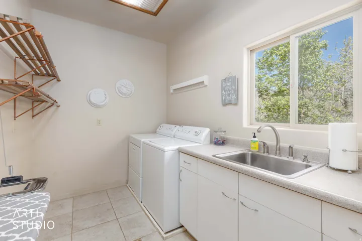 Utility room featuring a large window, a stainless steel sink, white cabinetry, and tile flooring