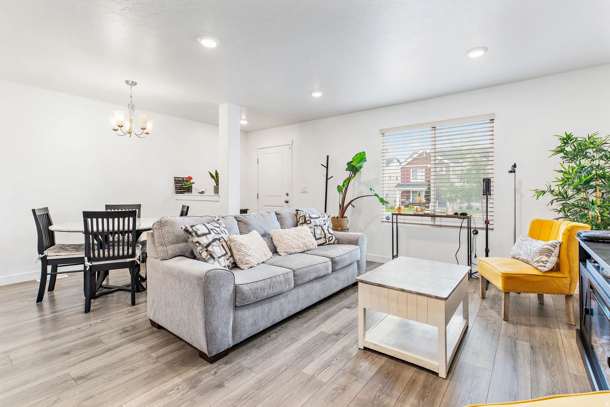 Open-concept living area featuring wood-finish flooring, recessed lighting, and a prominent window with blinds