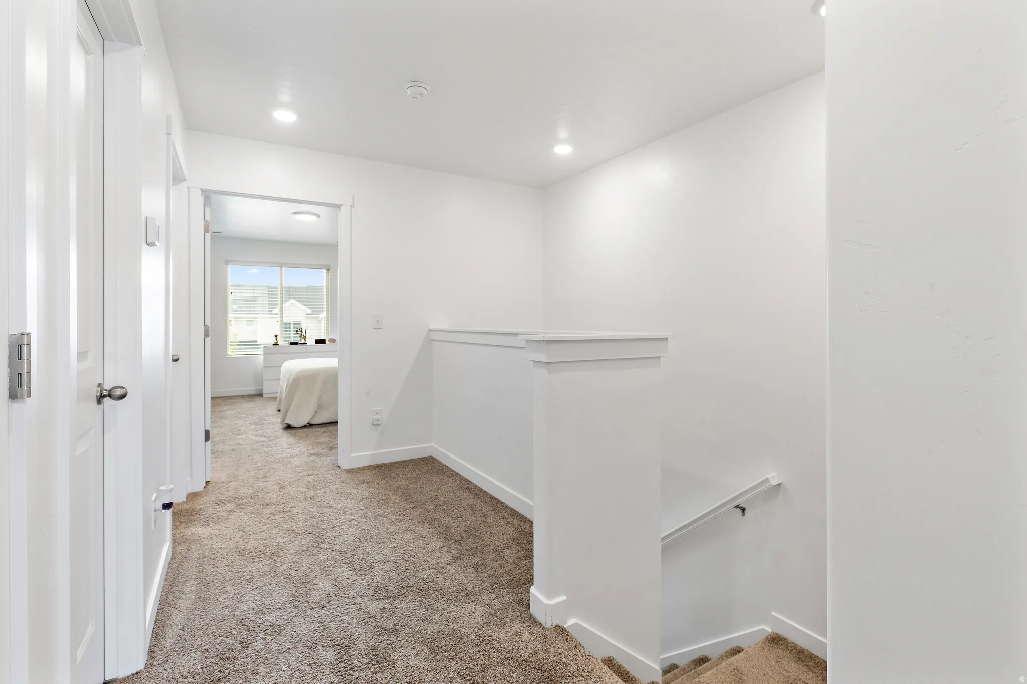 Carpeted hallway featuring white paneled doors, recessed lighting, and a staircase with a white handrail