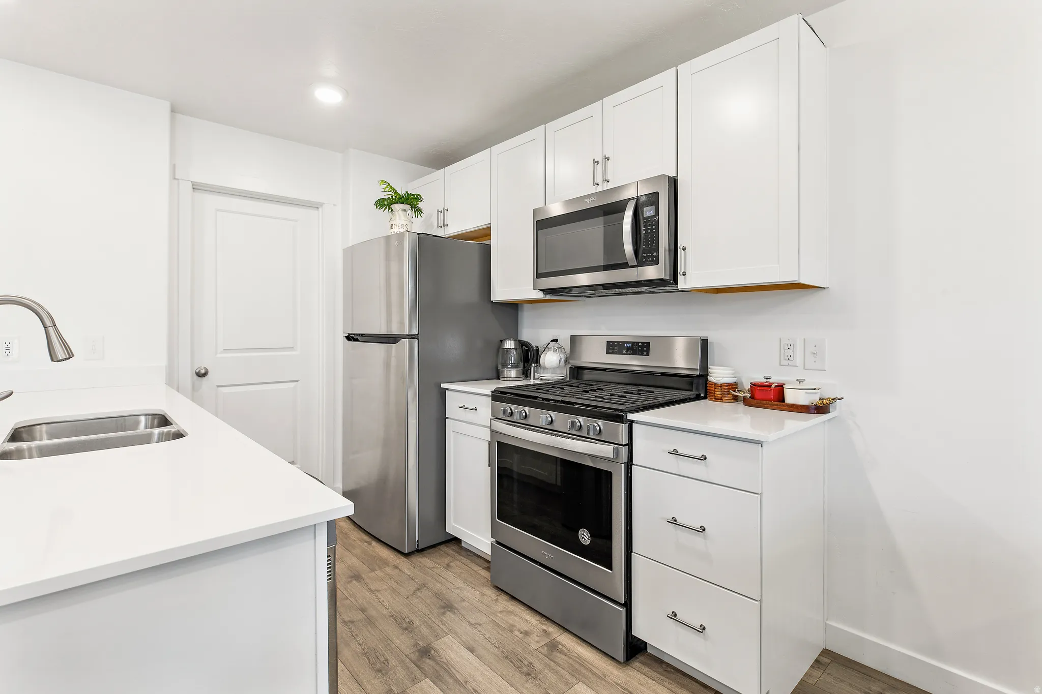 Modern kitchen featuring white cabinetry, stainless steel appliances, light-colored countertops, wood-finish flooring, and a double basin sink with a gooseneck faucet