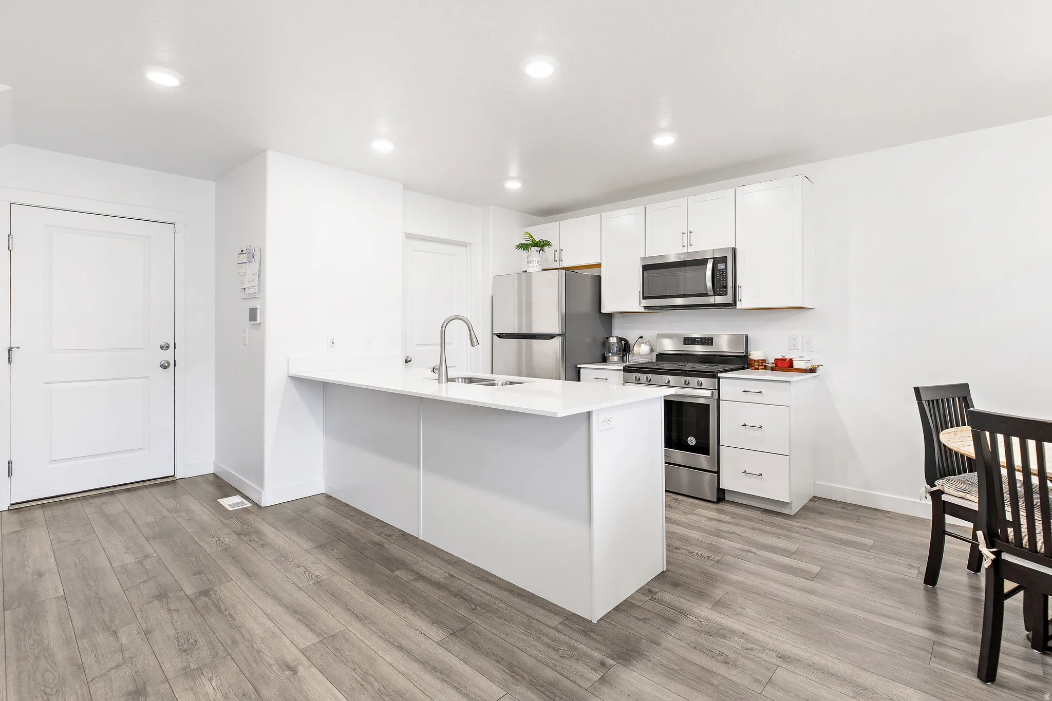 Modern kitchen featuring white cabinetry, stainless steel appliances, a white island with sink and faucet, recessed lighting, and wood-finish flooring