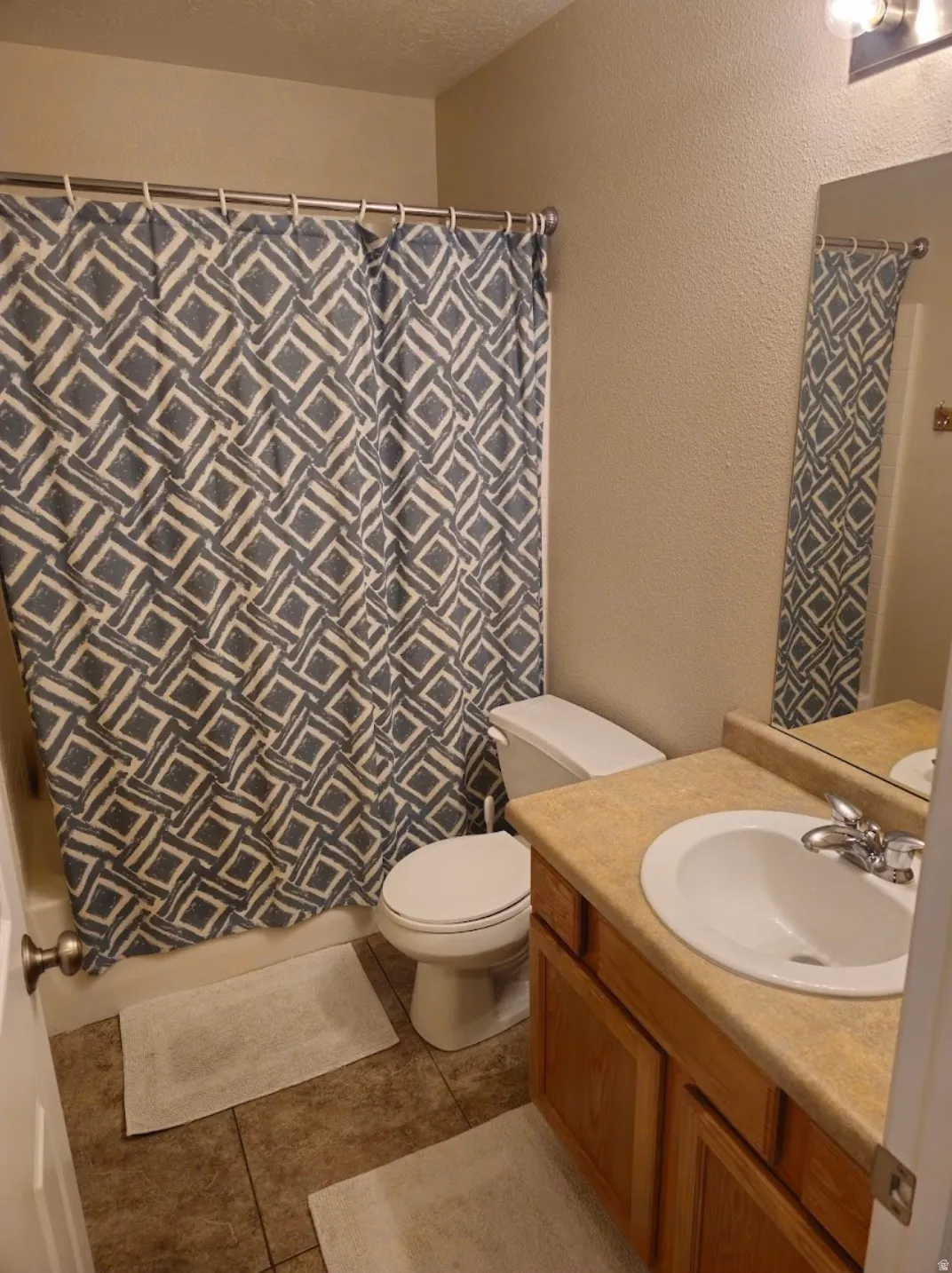 Bathroom featuring a single vanity with wood-finish cabinetry, a drop-in sink, and a light-toned countertop