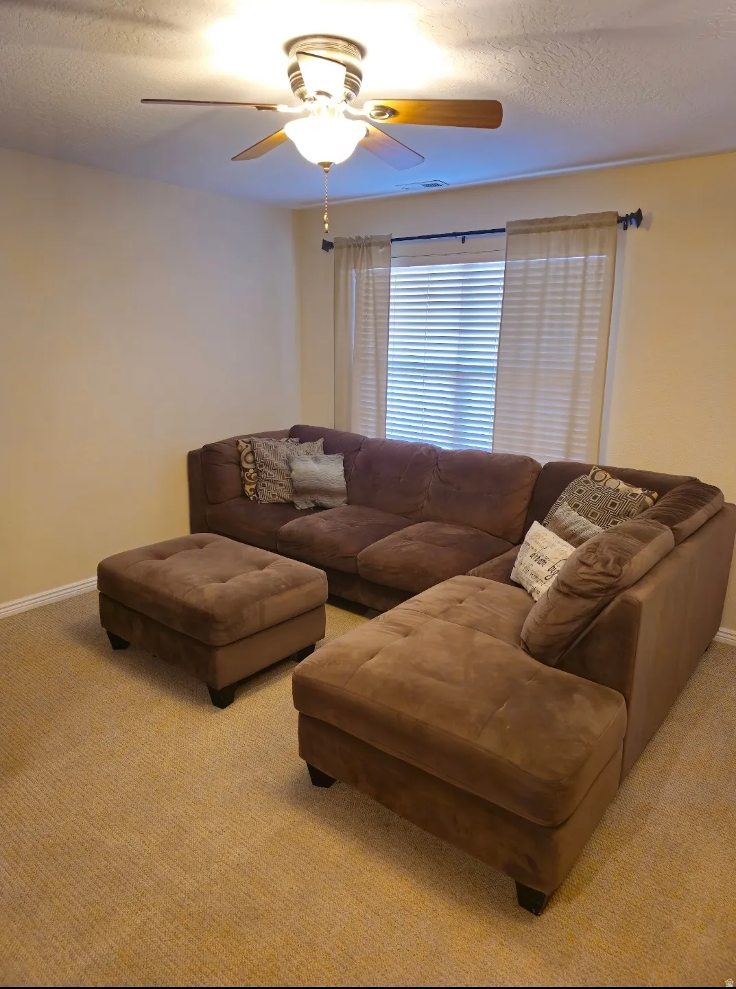 Neutral wall paint, ceiling fan with light fixture, window with blinds, and light-colored carpet flooring