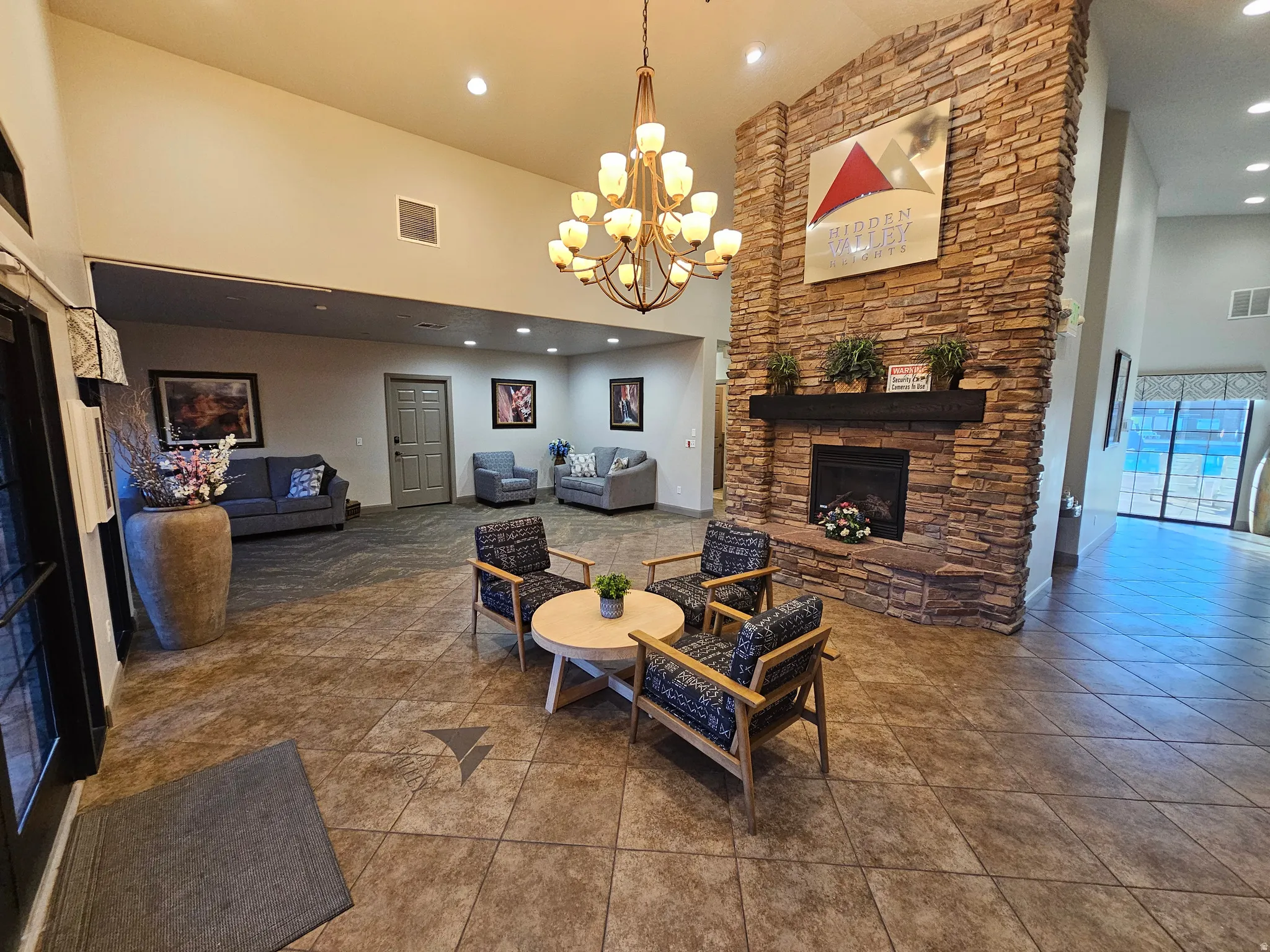 Spacious common area featuring a stone fireplace, high ceilings, large-format tile flooring, and a chandelier lighting fixture