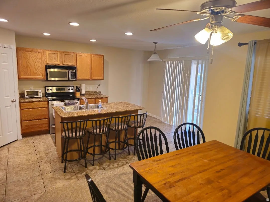 Kitchen featuring recessed lighting, a central island with a sink and counter seating, stainless steel appliances, and wood cabinetry