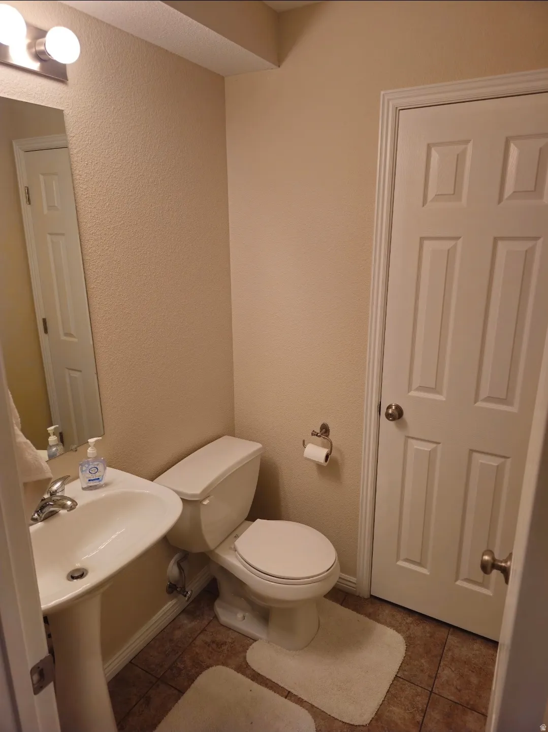 Pedestal sink with chrome faucet, a white toilet, and tile flooring